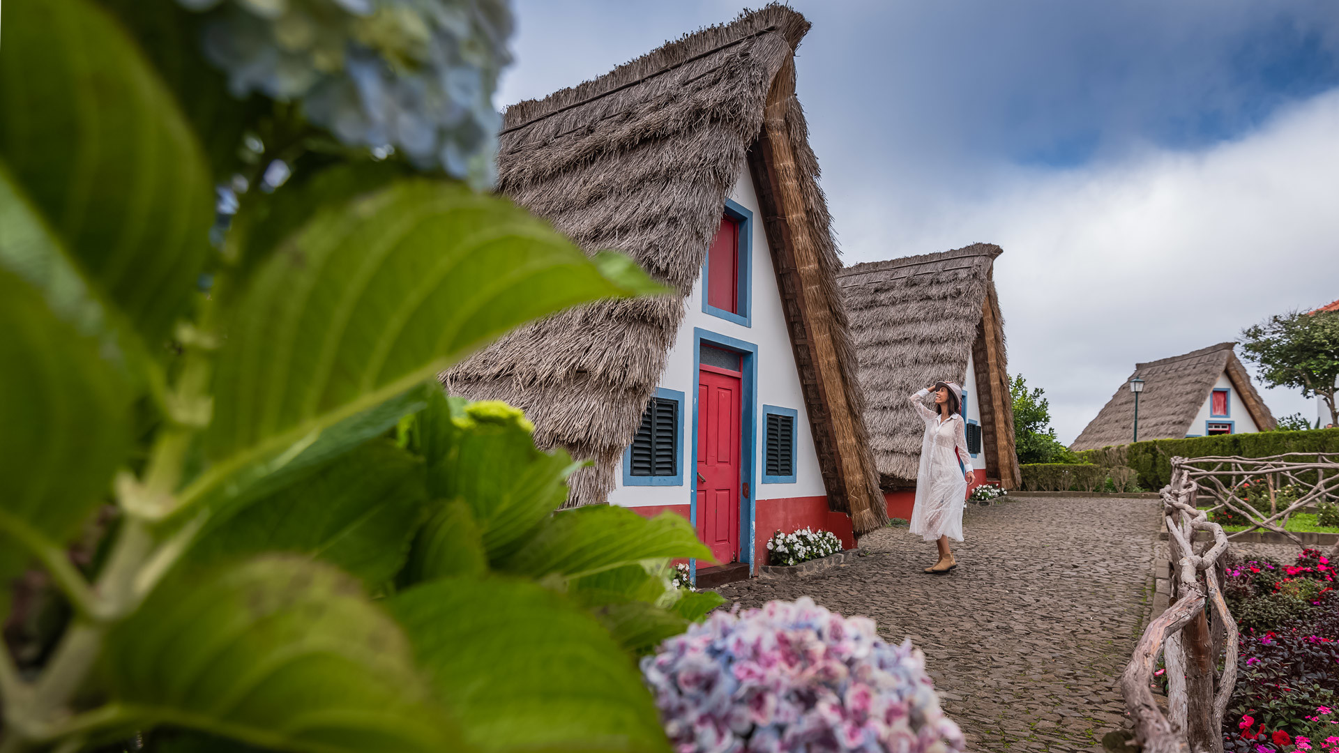 Woman in white dress near triangular house with thatched roof.