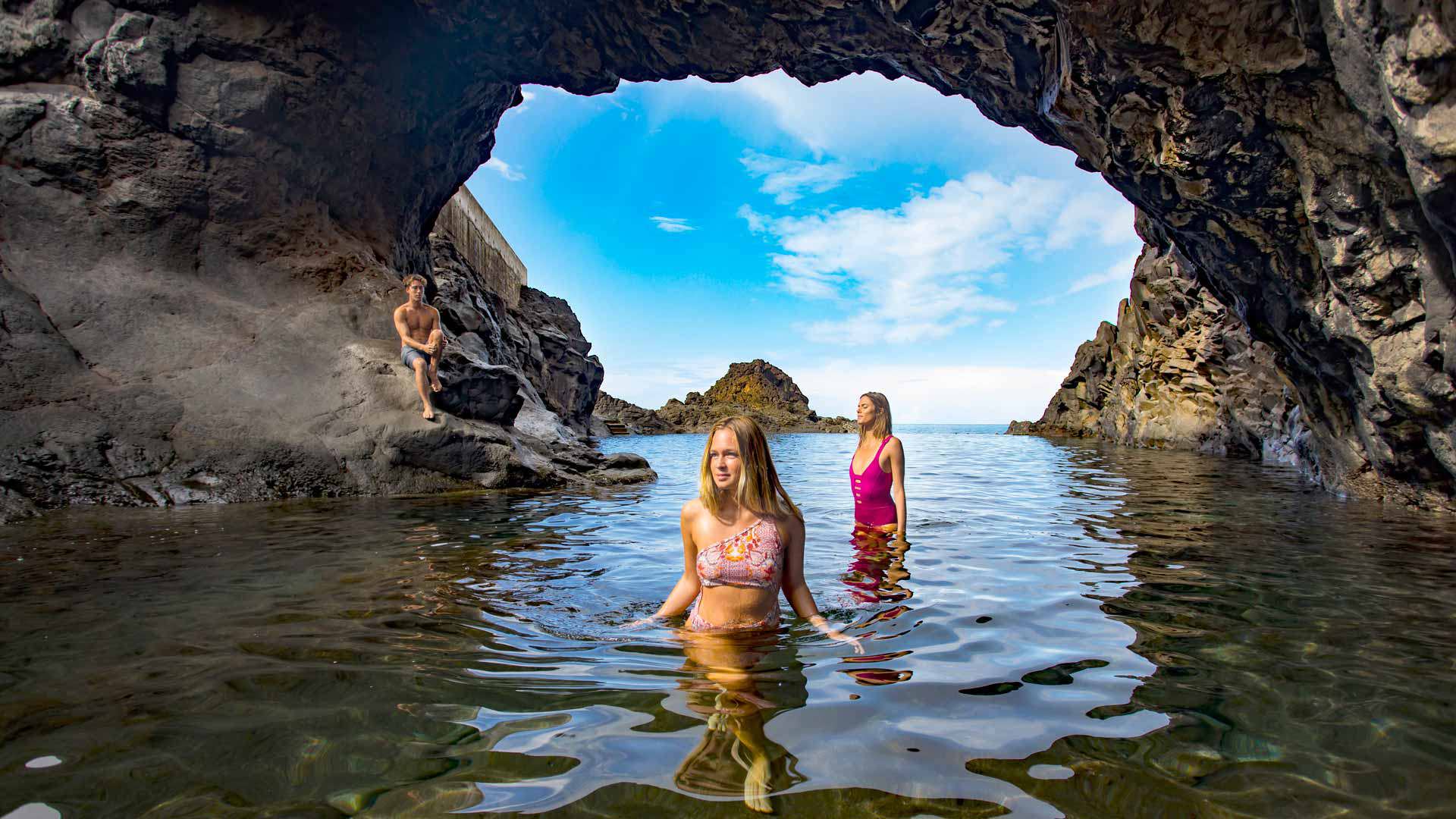 Boy sitting on a rock and two girls in the water of the natural pool in Madeira.