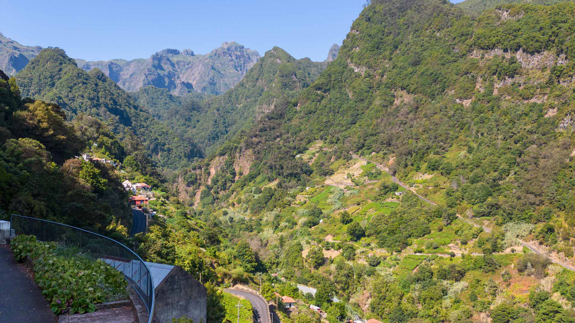 Zaun mit Blick auf ein Tal und Häuser zwischen Bergen.