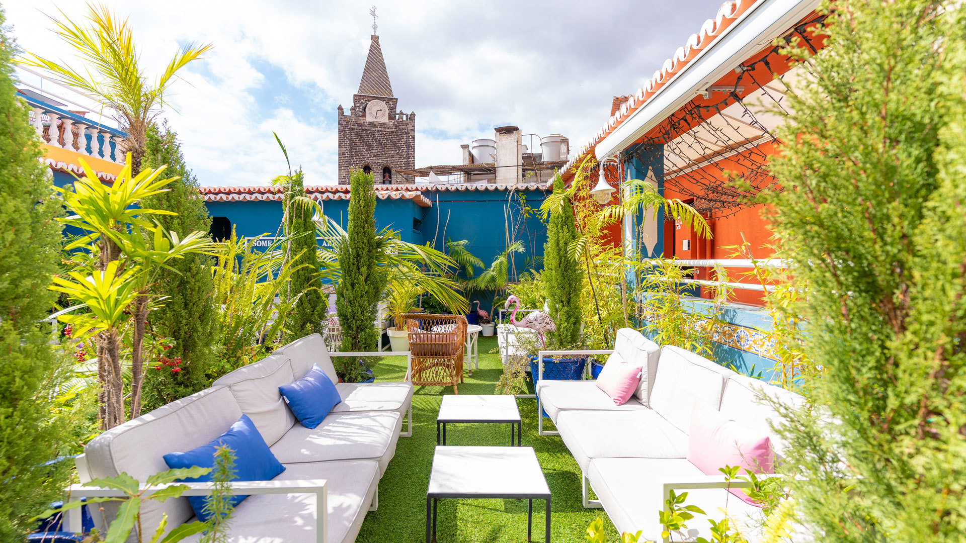 Sofás e plantas com torre de igreja visível ao fundo.