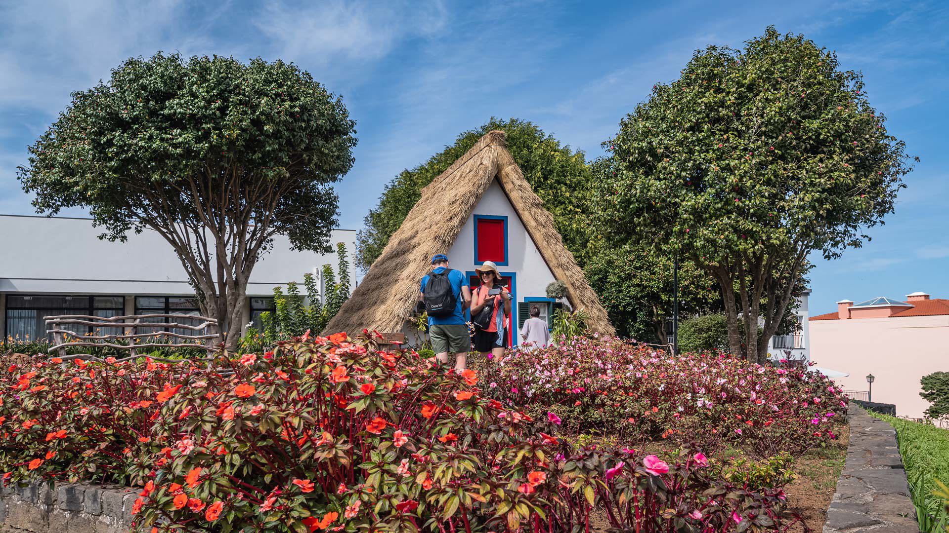 Triangular house surrounded by trees, garden, and red flowers in Madeira.