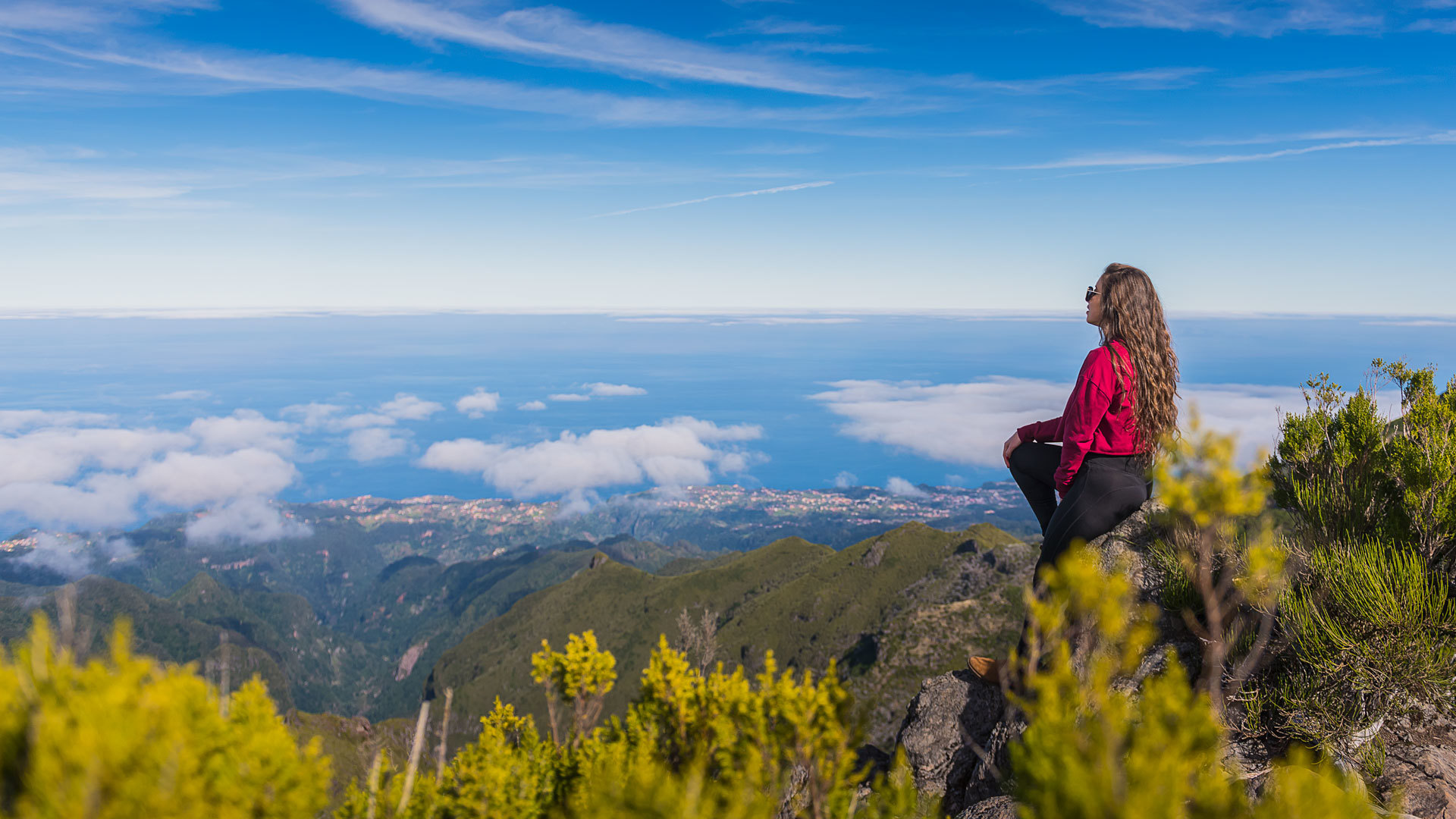 Mujer sentada en roca con vista a montañas y mar en Madeira.