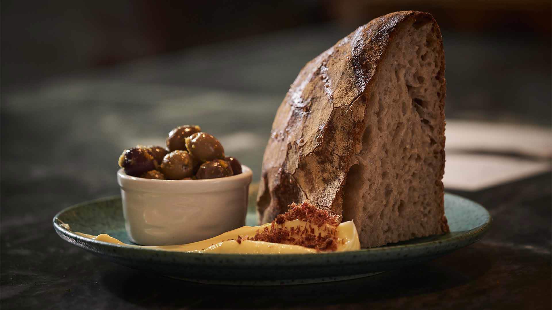 Prato com pão, manteiga e azeitonas numa taçinha.