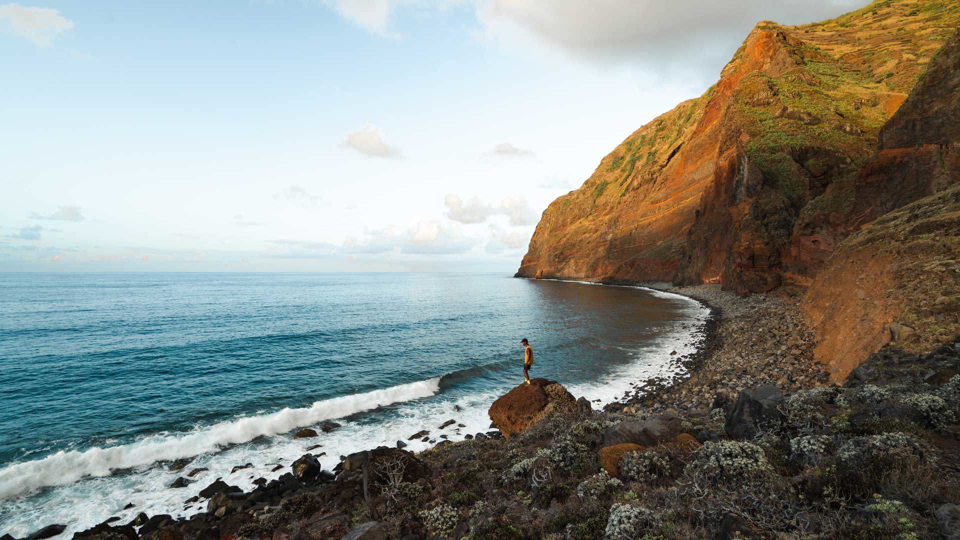 Man by the sea and rocks on the sunlit hillside in Madeira.