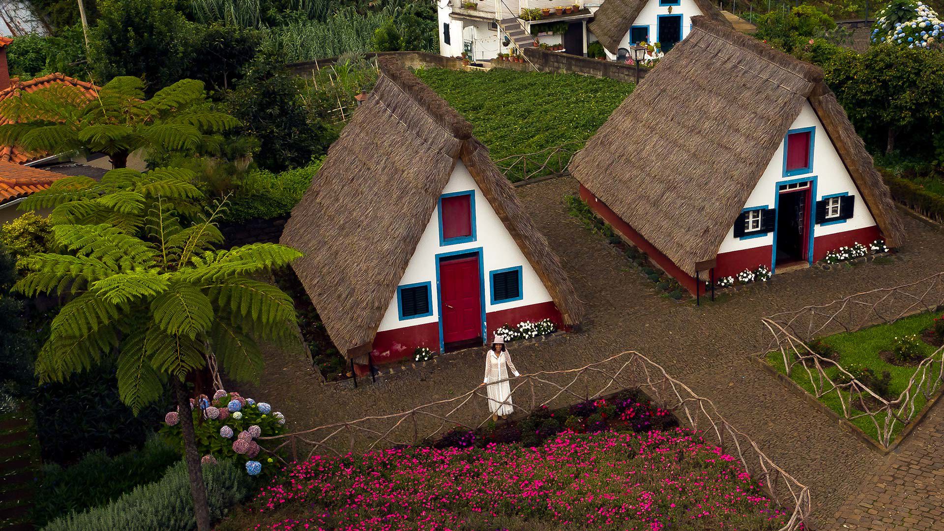 Woman in white dress near triangular houses with thatched roofs.