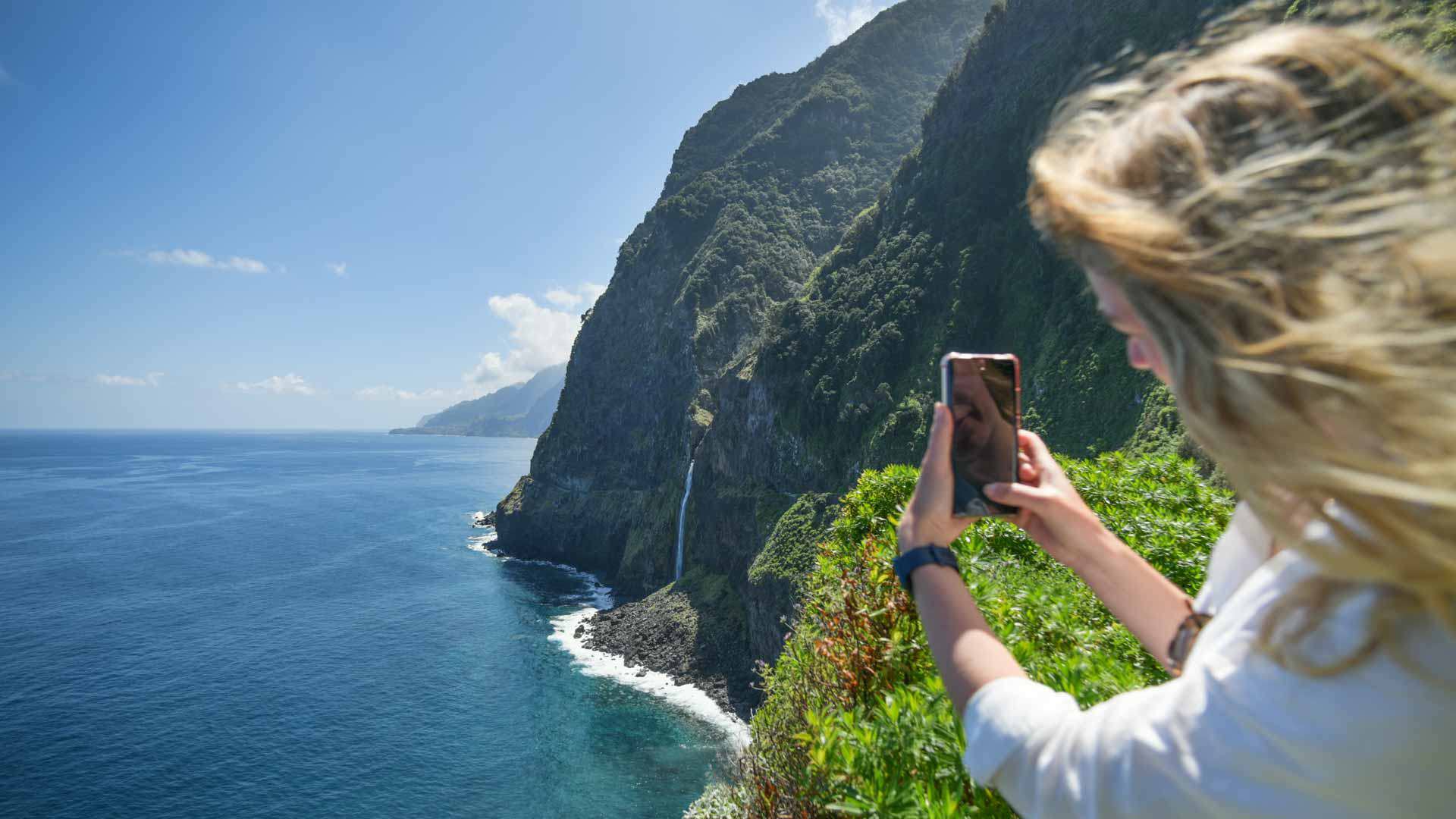 Mujer tomando foto en mirador con cascada en el paisaje de Madeira.