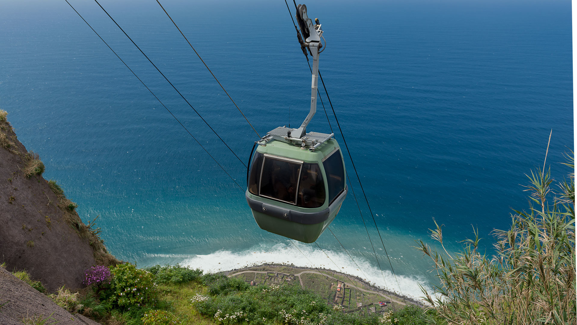 Cable car crosses slope with sea view.