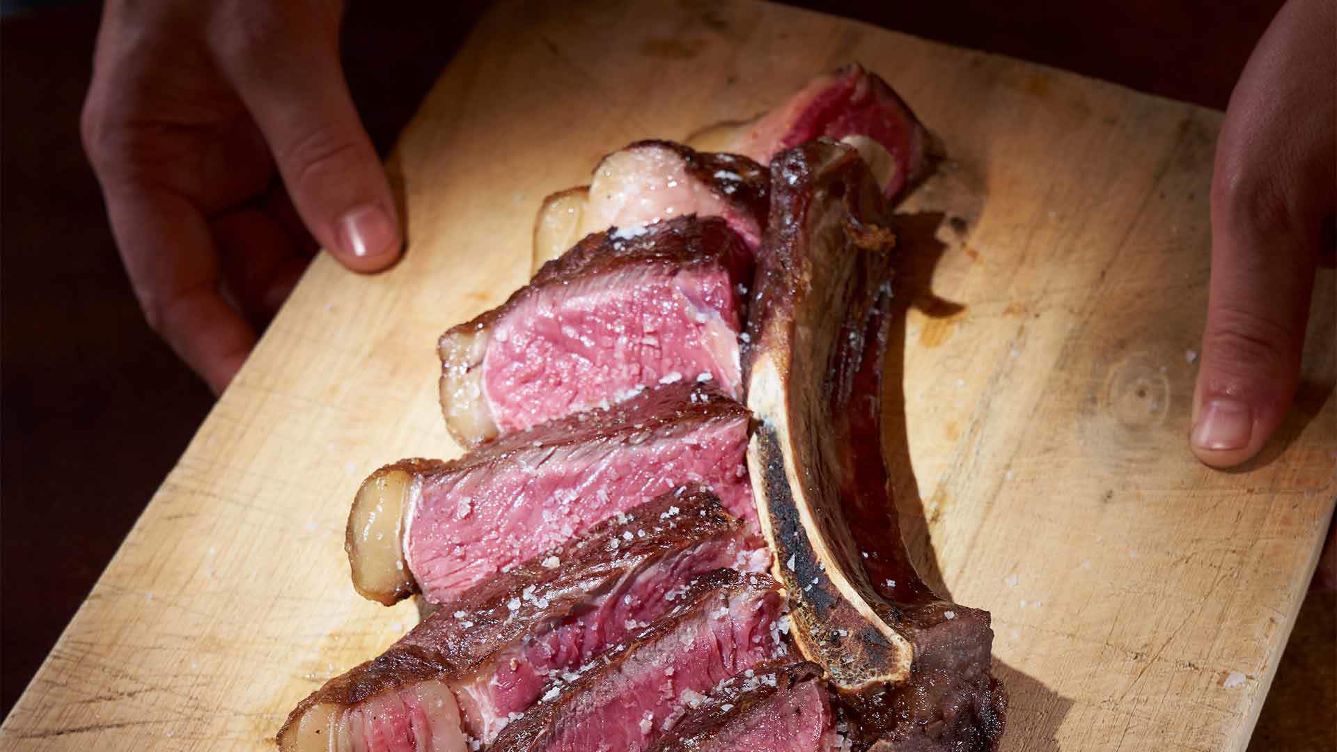 Tábua de madeira com carne fatiada por cima.