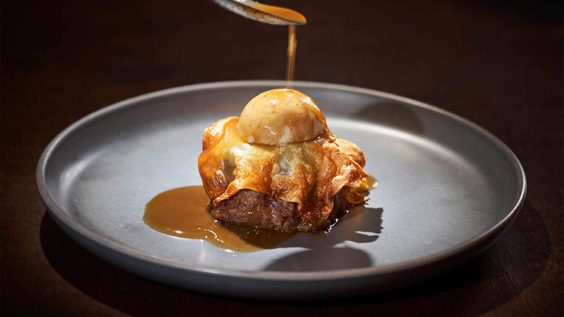 Prato com bife coberto a ser regado com molho.