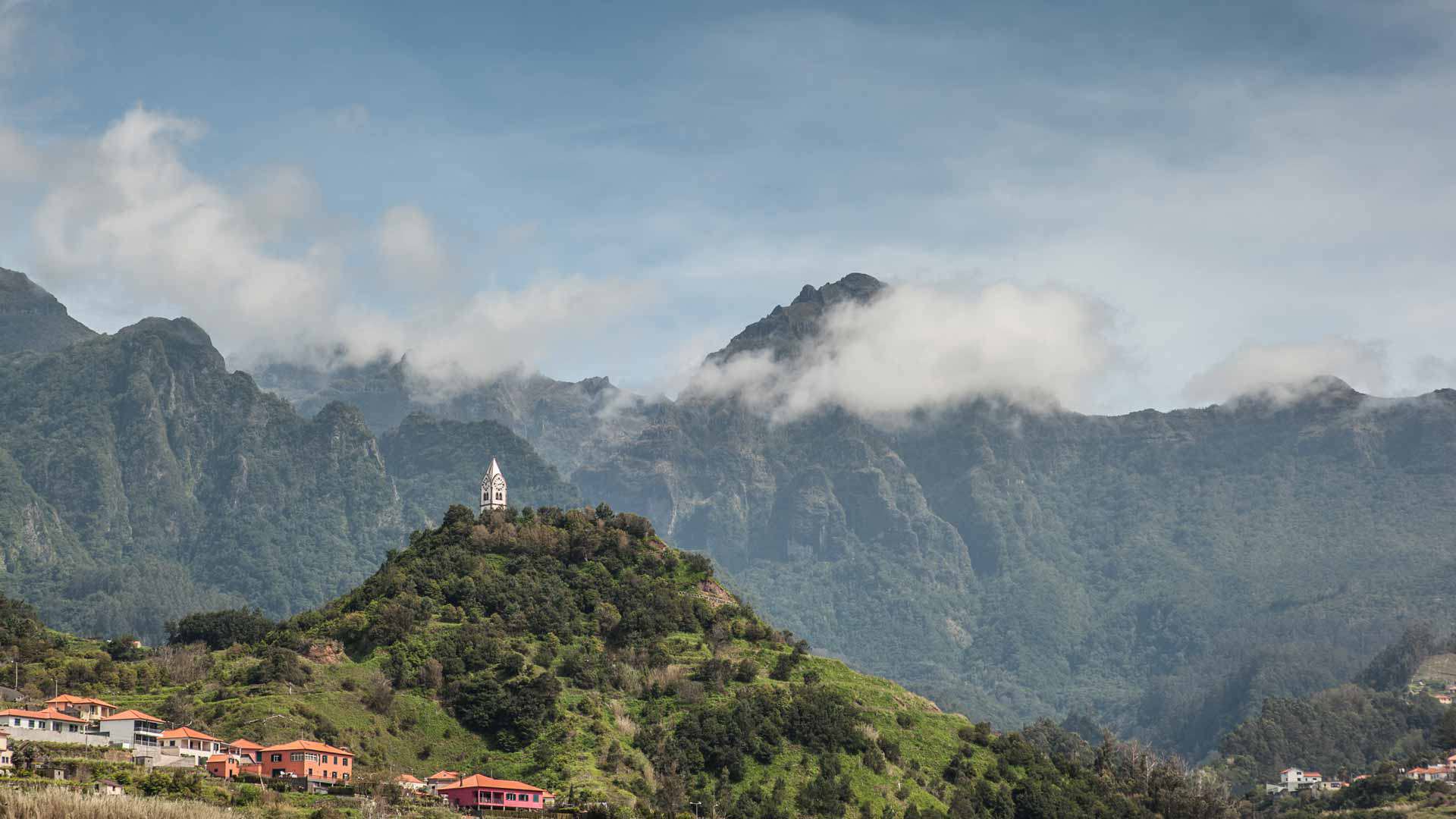 Church atop a peak surrounded by green mountains.
