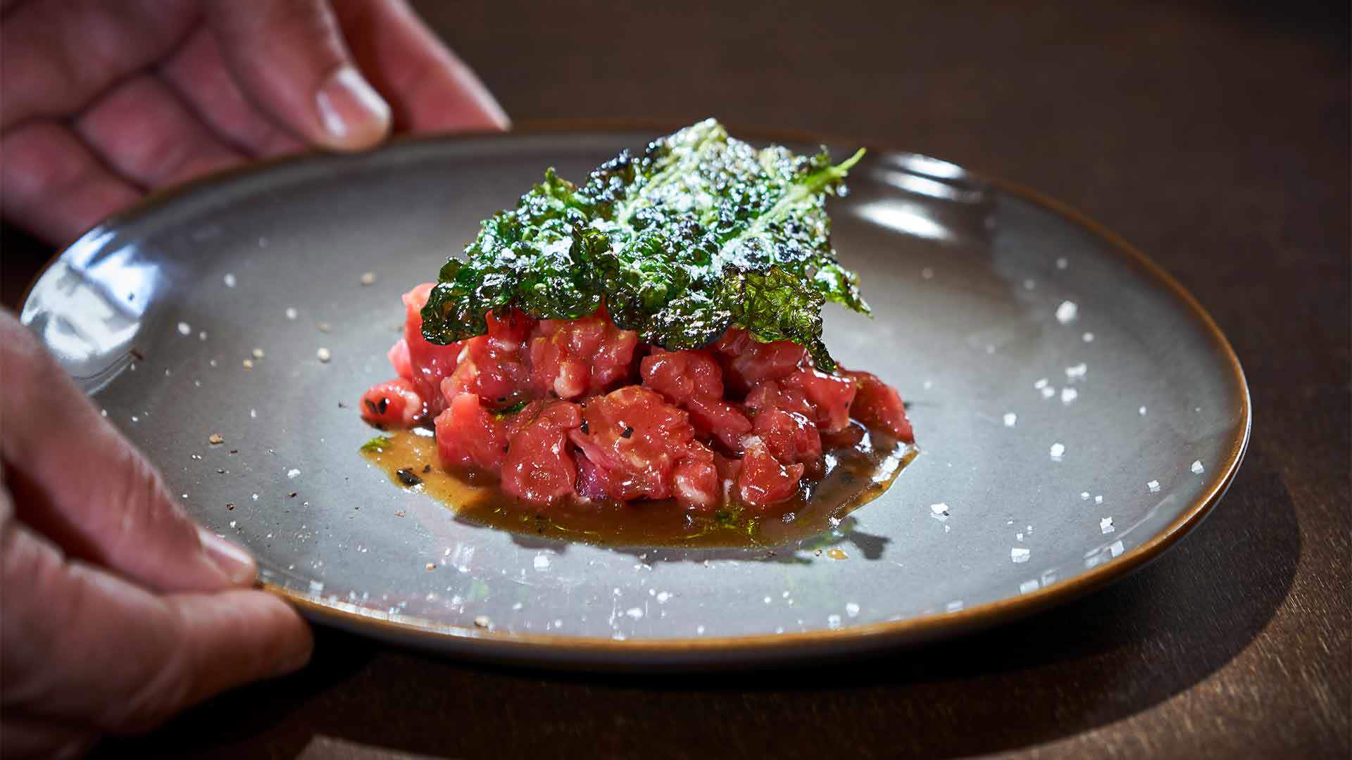 Prato com tártaro de carne e vegetais por cima.