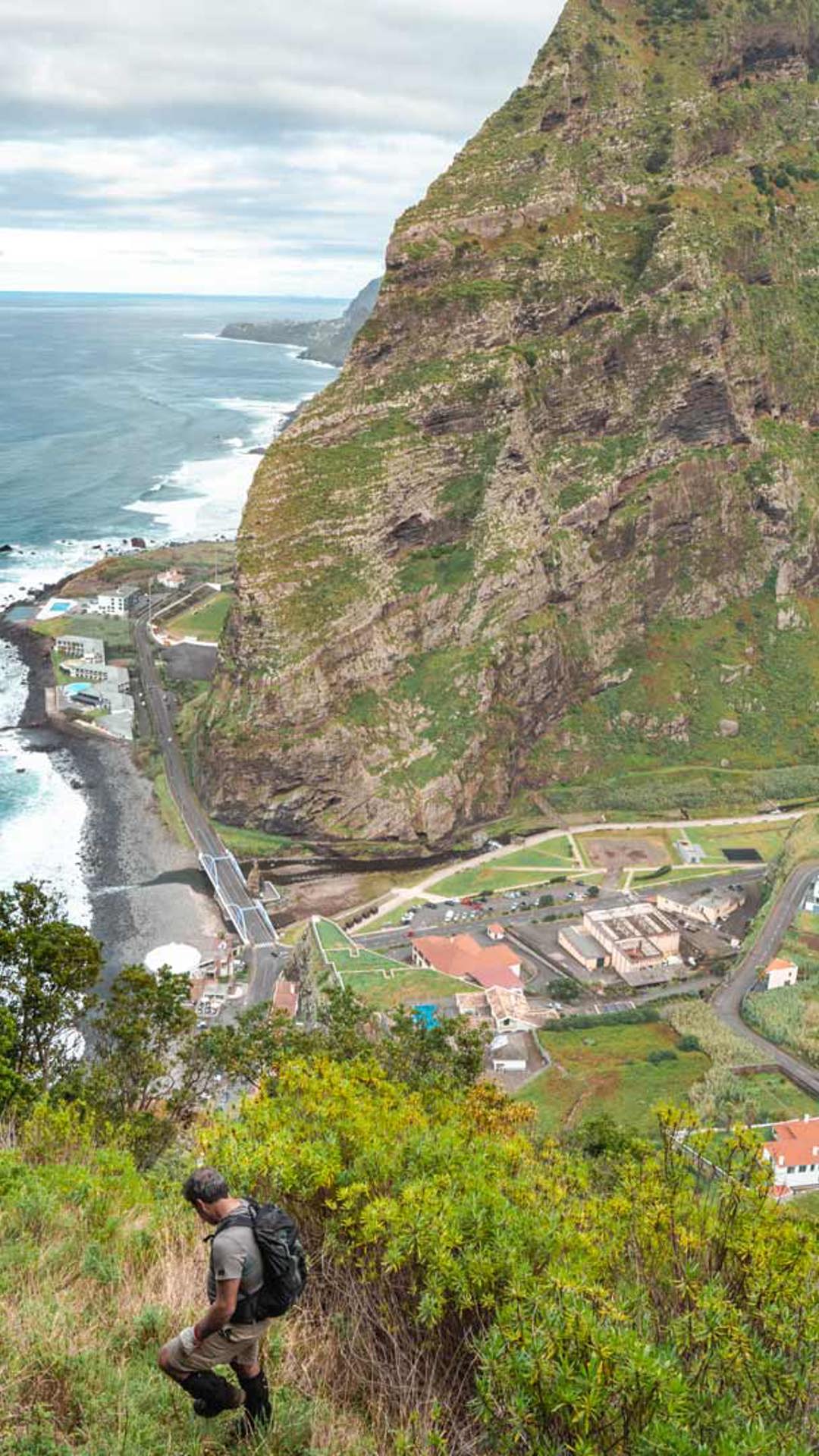 Vallée avec maisons et montagne, mer avec vagues en arrière-plan.