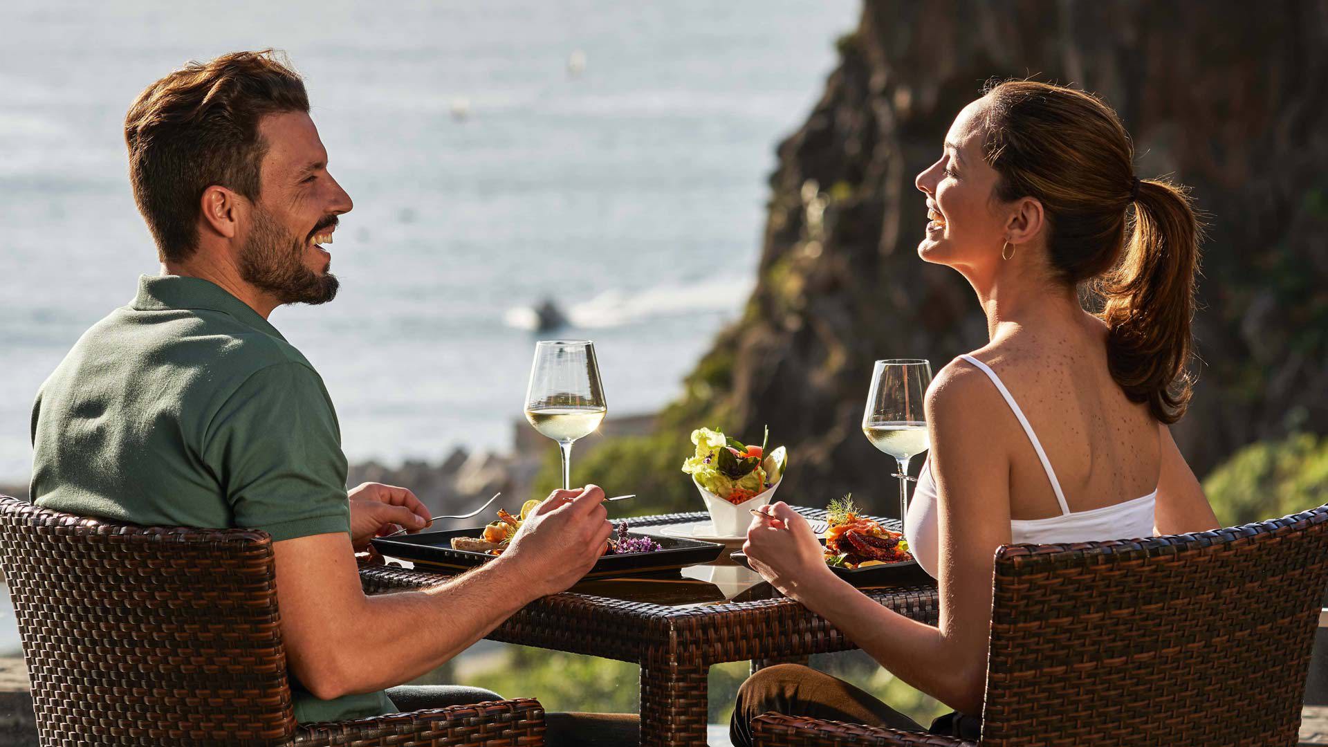 Couple enjoying a meal with a view of the sea and mountains.