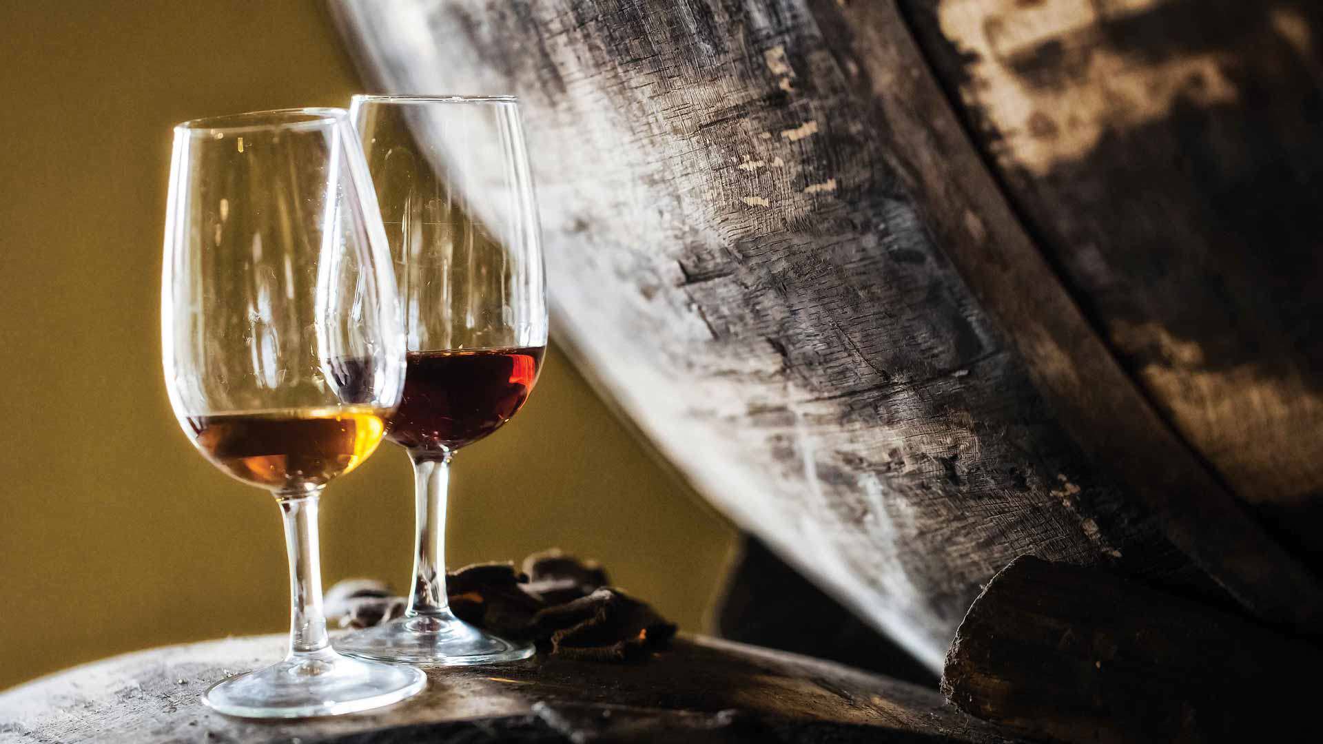 Zwei Gläser Madeirawein neben einem Weinfass.