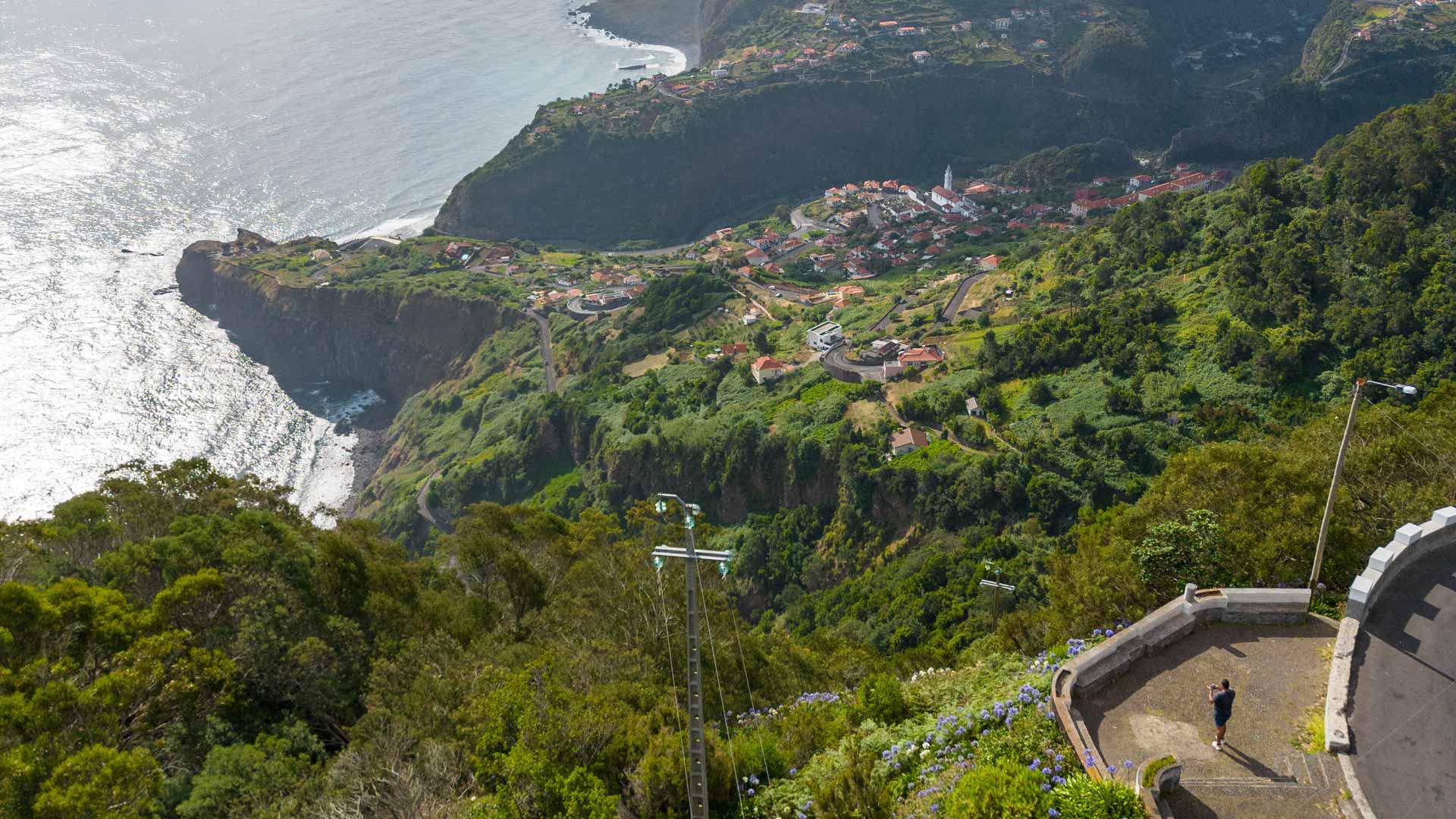 Green hillside with houses and sea view.