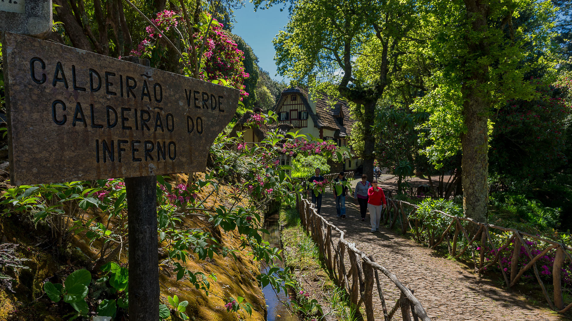 Pessoa com casaco vermelho perto de placa informativa e vedação de madeira na natureza.