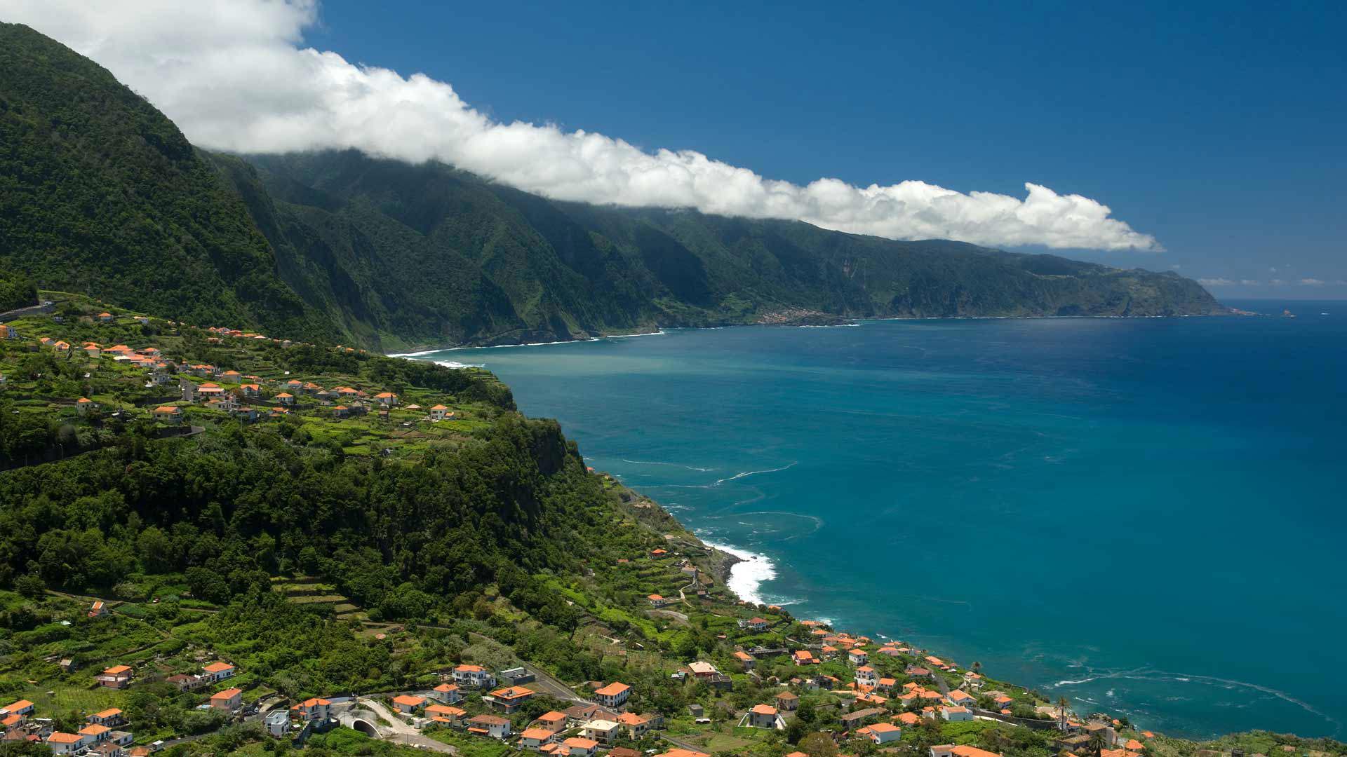 Encosta com casas junto ao mar e nuvens na Madeira.