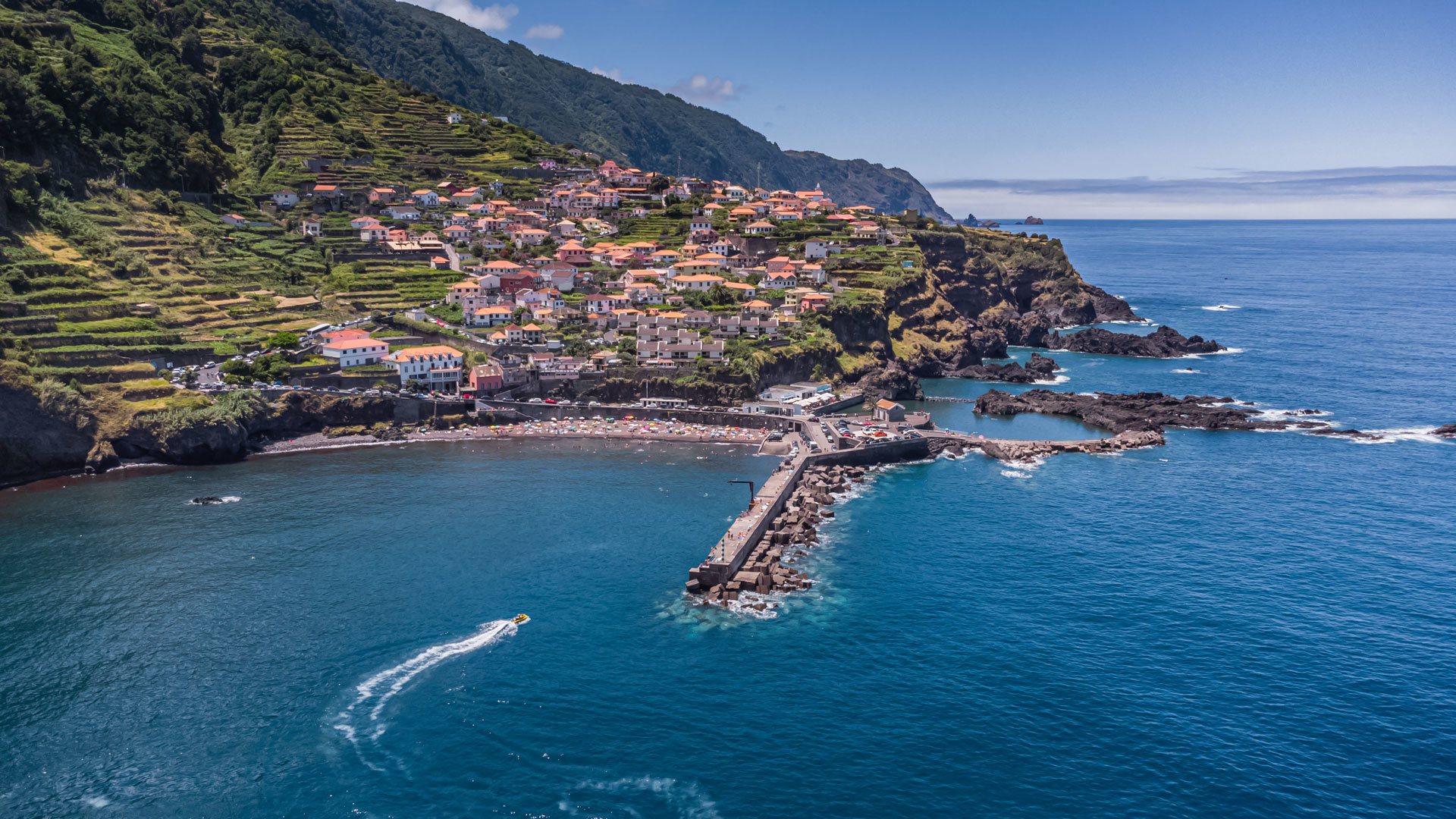 Strand mit Steg, Häusern am Hang und Berg im Hintergrund auf Madeira.