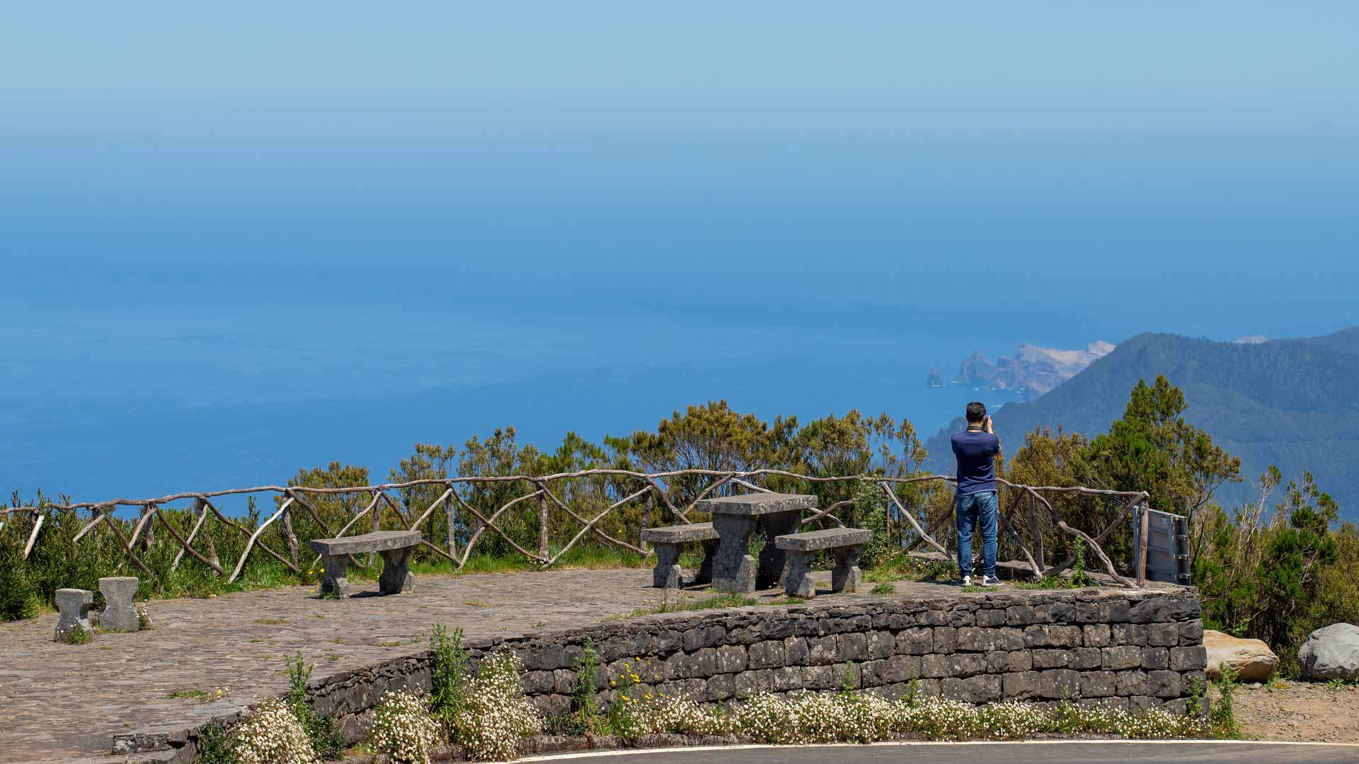 Persona en mirador de piedra con vista al mar y montañas.