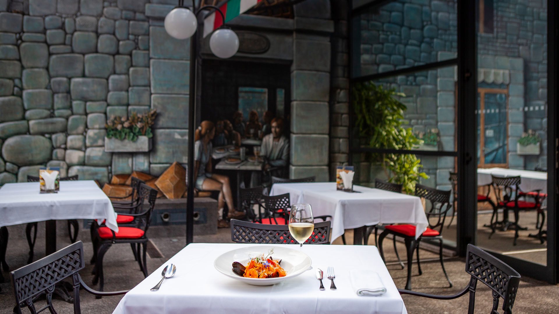 Tische auf der Terrasse mit Teller, Besteck und Glas Weißwein.