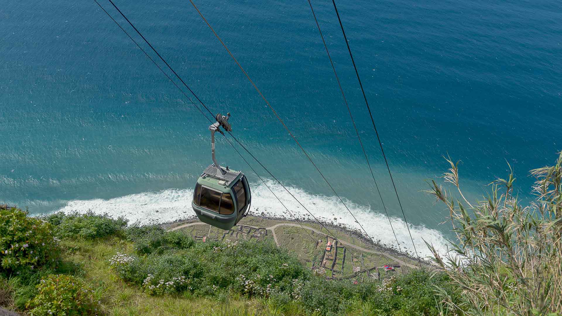Seilbahnkabine über steilem Hang mit Meerblick auf Madeira.