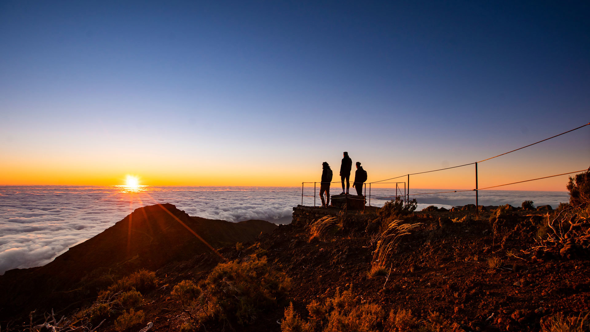 Trois personnes au coucher du soleil parmi les nuages dans les montagnes de Madère.