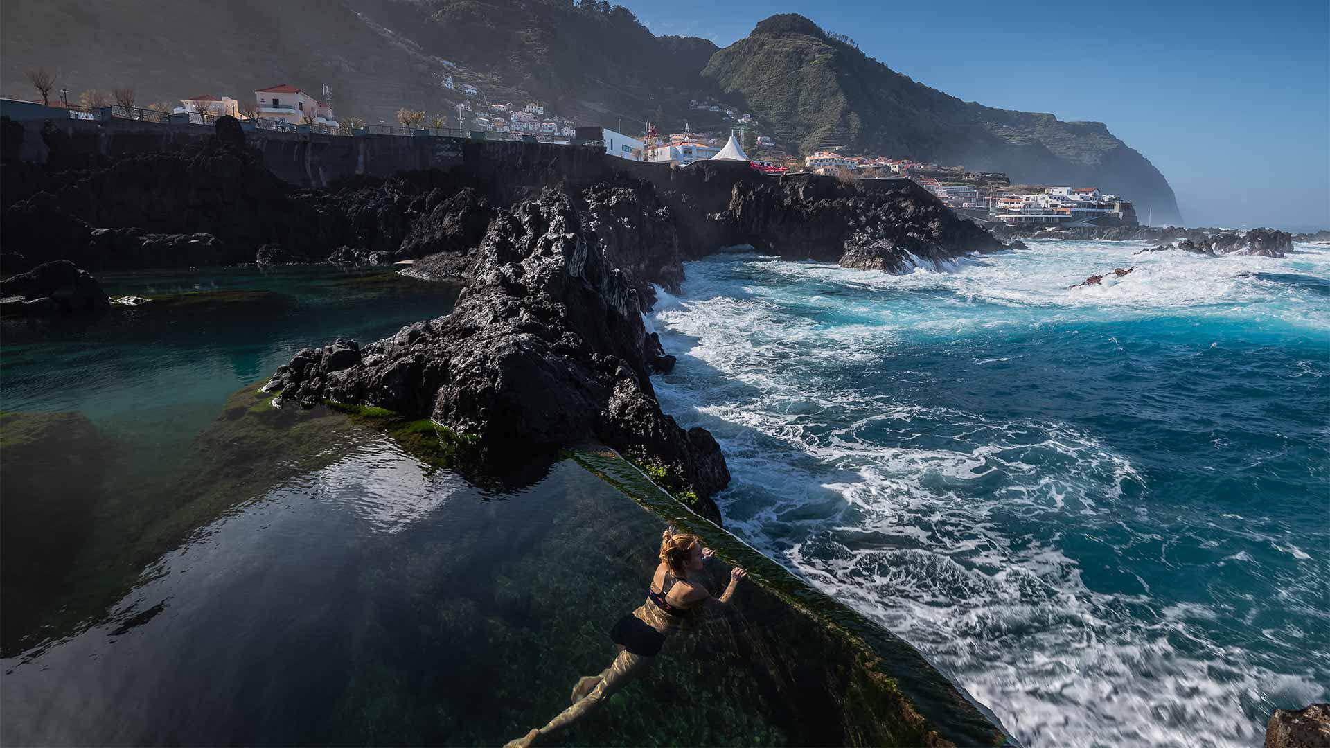 Pessoa numa piscina natural a ver a paisagem de mar e rochas na Madeira.