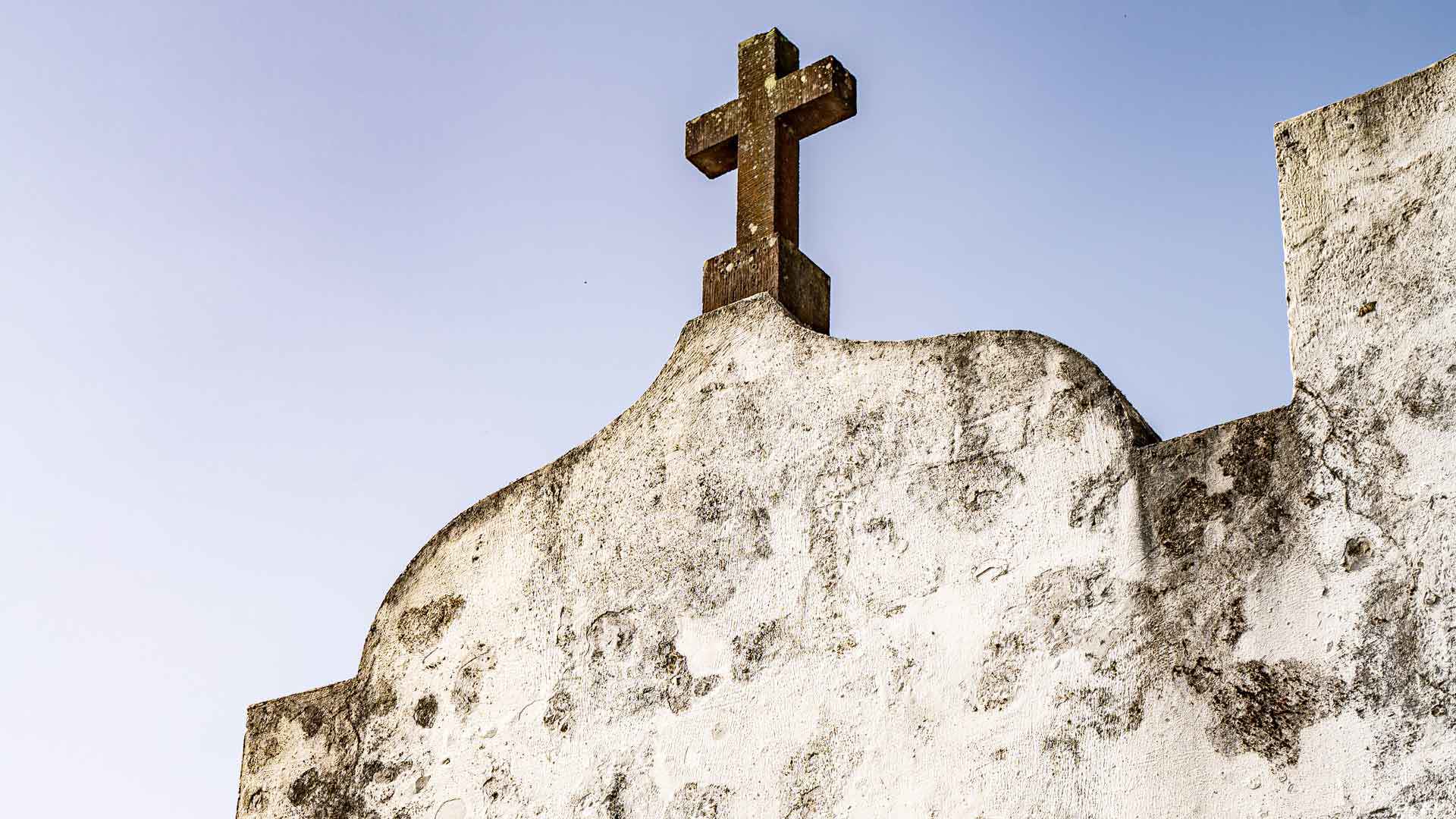 Croix au sommet d’une chapelle avec ciel en arrière-plan.