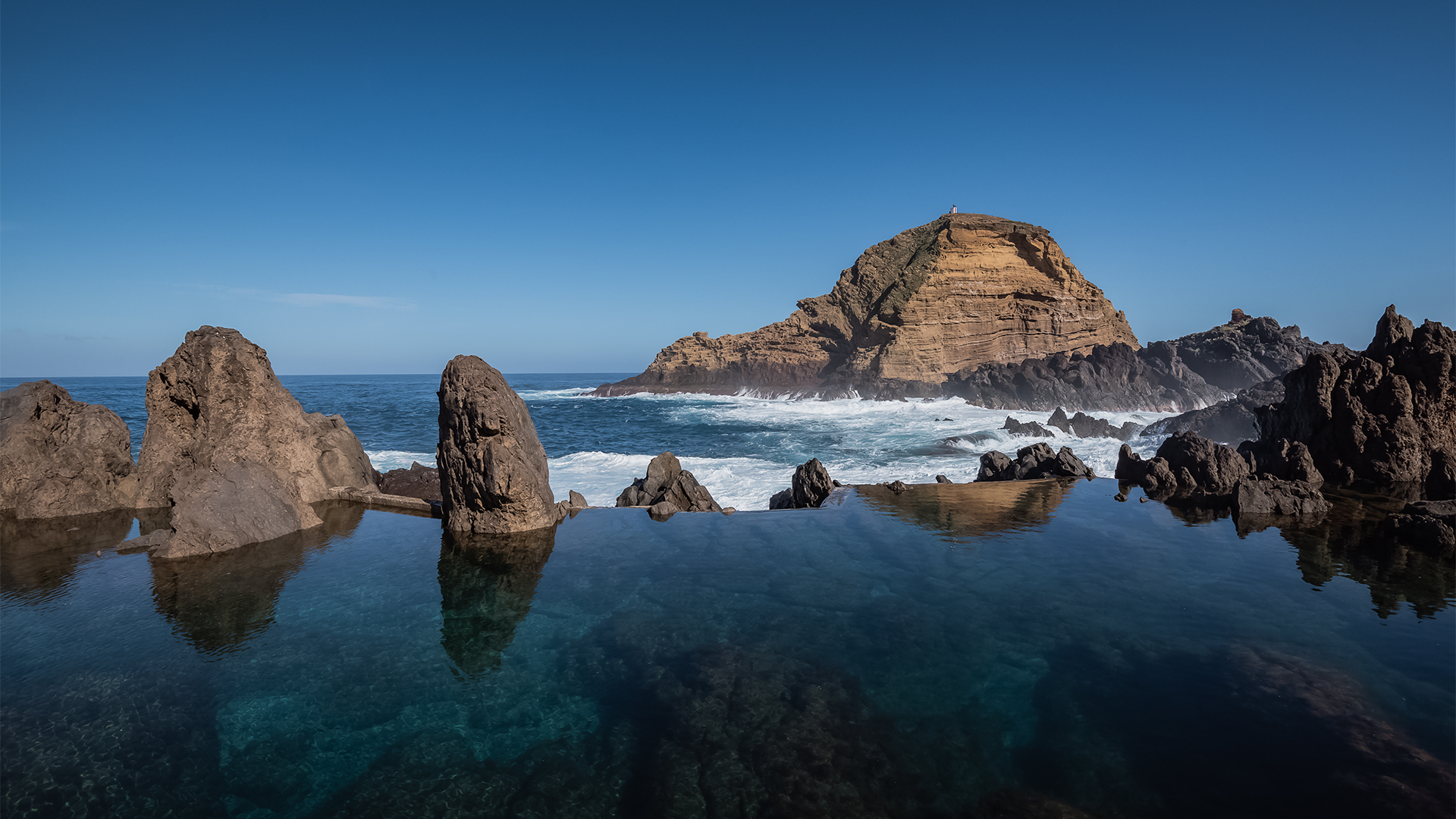 Natural pool by the sea among rocks, with a large rock in the scene.