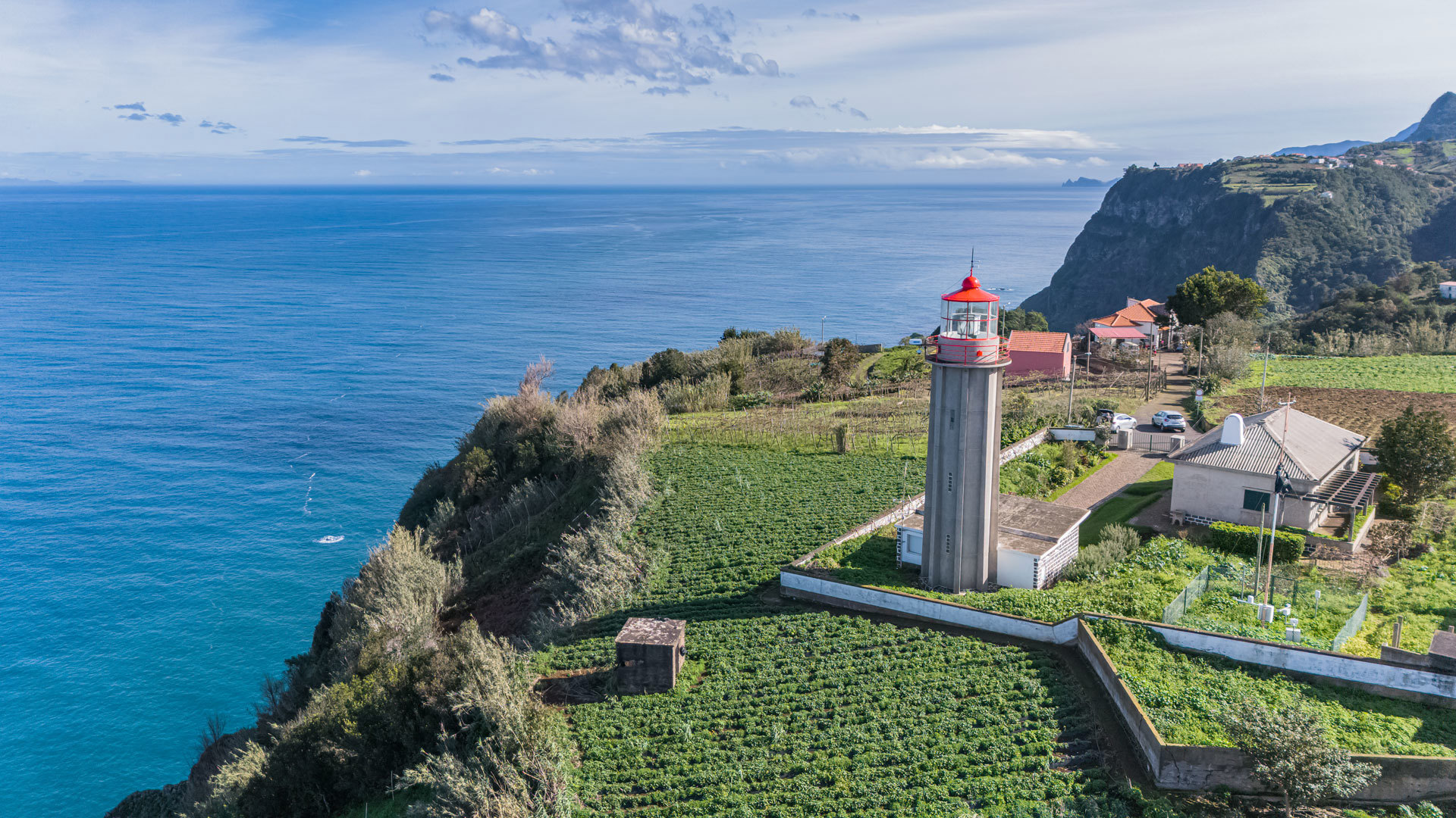 Lighthouse on hillside with green fields and sea in Madeira.