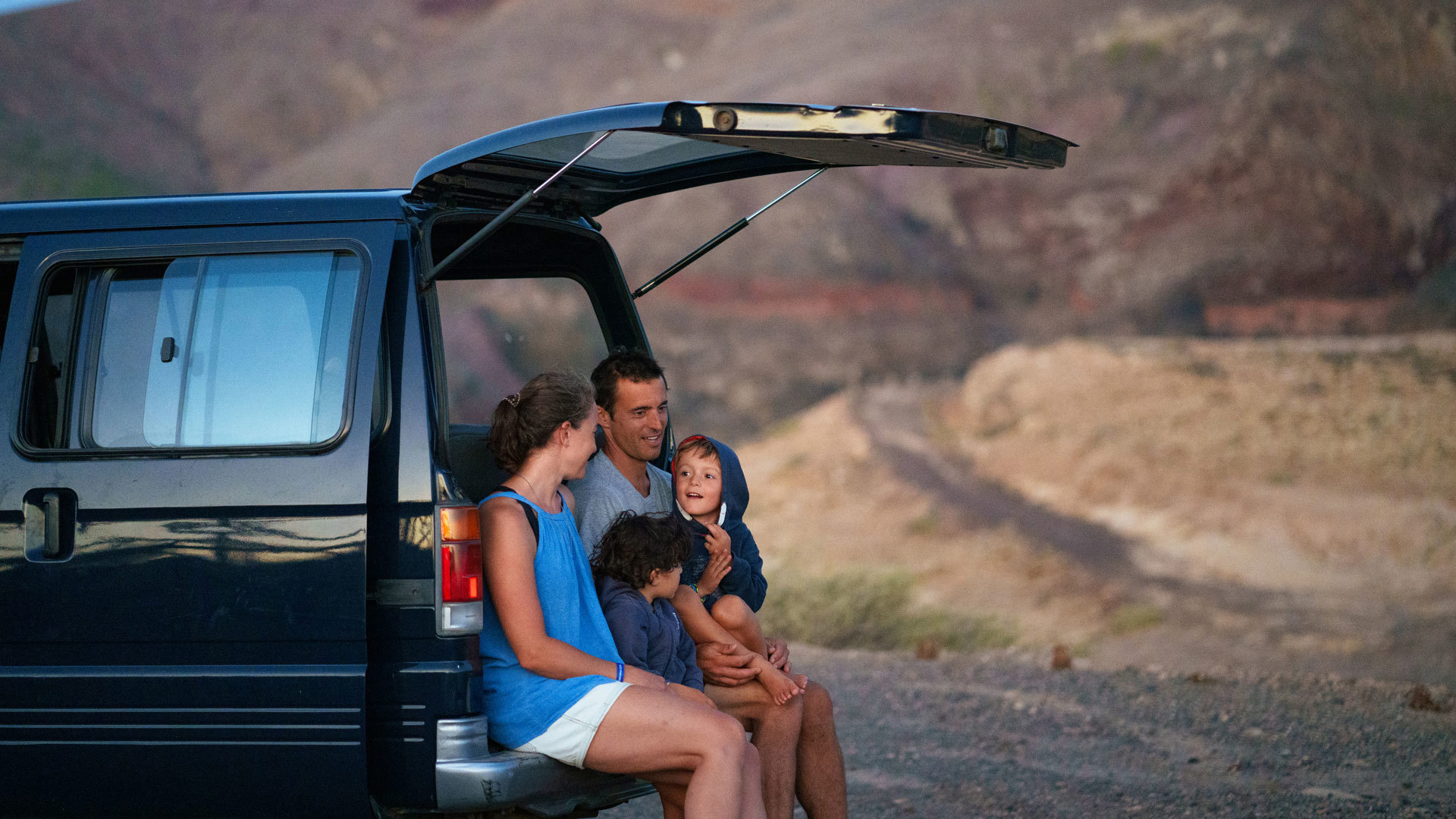 Family sitting on the back of a car in Porto Santo with mountain in the background.