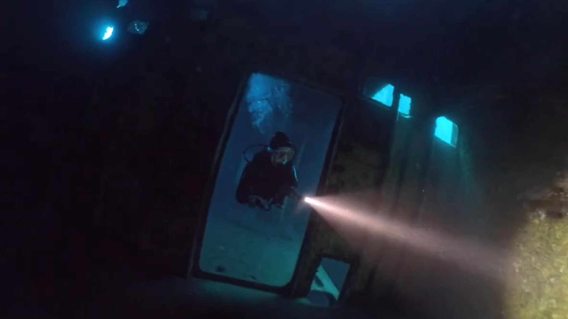 Mergulhador com lanterna a explorar um navio afundado.