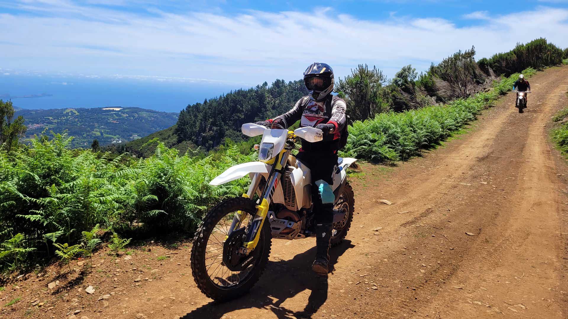 Persona montando una moto de tierra en un paseo de enduro, con paisaje alrededor.