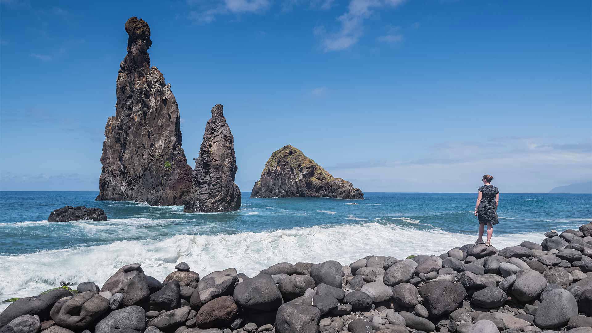 Mujer junto a formación rocosa y piedras en la orilla del mar en Madeira.