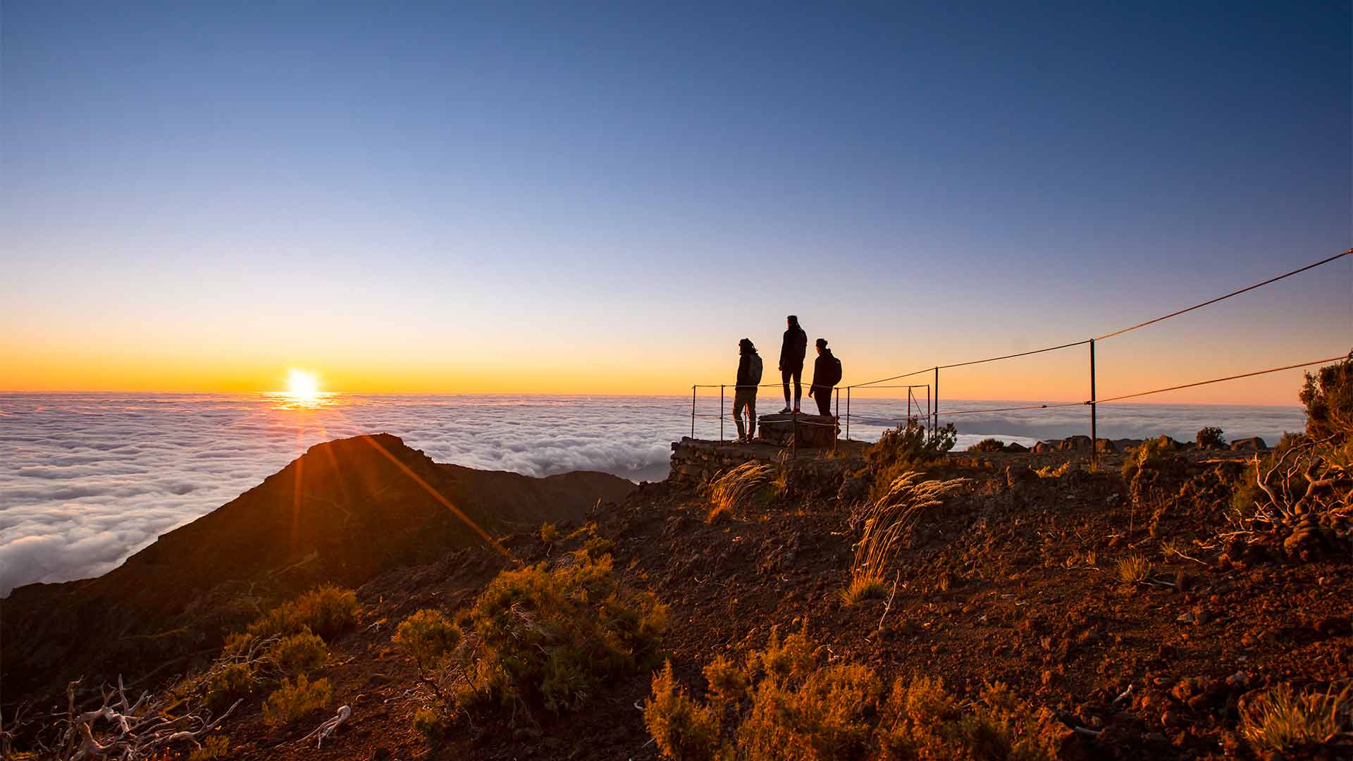 Drei Personen bei Sonnenuntergang zwischen Wolken in den Bergen Madeiras.