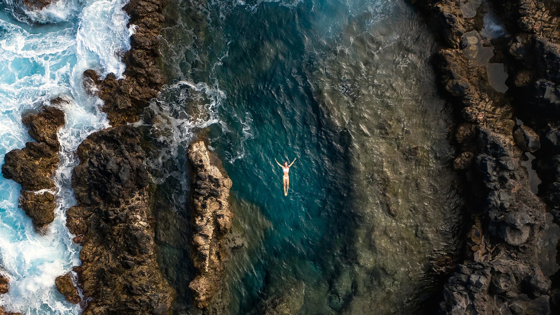 Mujer en las piscinas naturales de Porto Moniz junto al mar y las rocas.