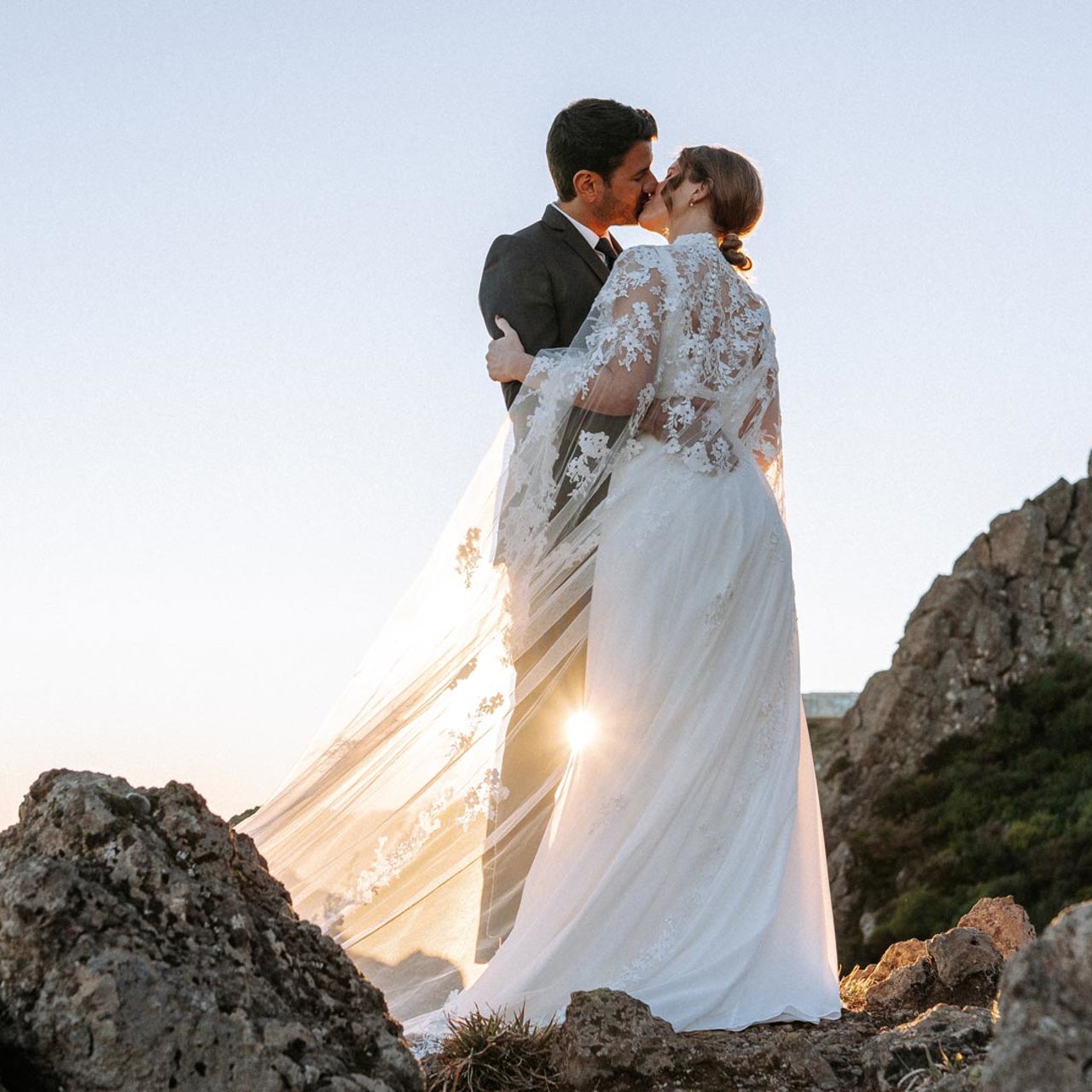 Couple in wedding attire in the mountains above the clouds, kissing.