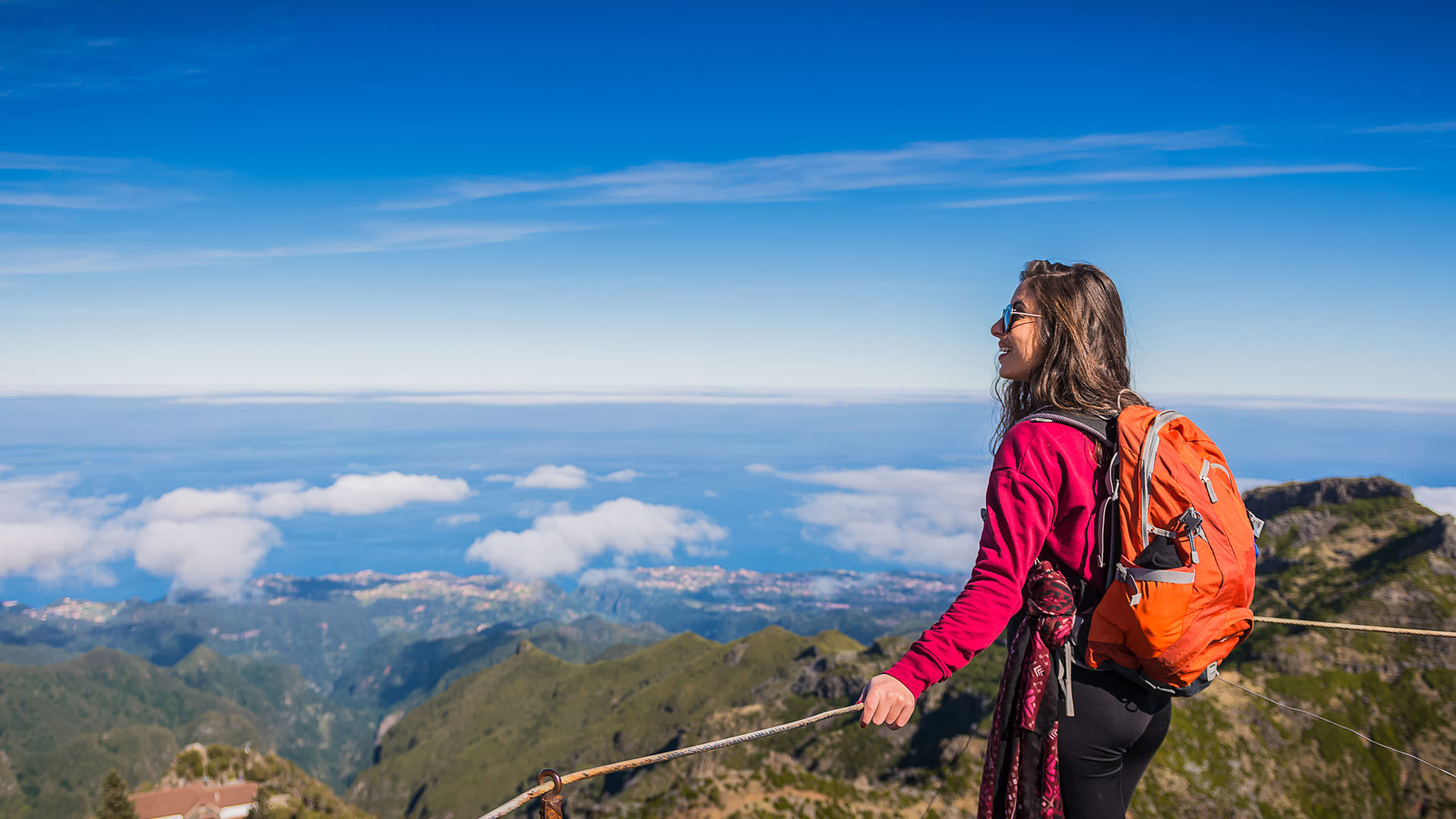 Woman in pink jacket and orange backpack at a viewpoint in Madeira.
