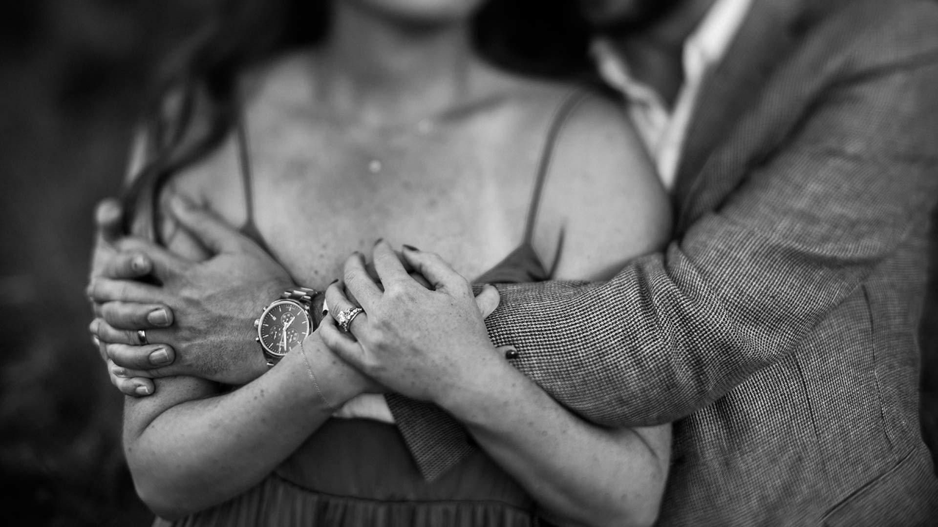 Couple embracing in a black and white photo, showing an engagement ring.