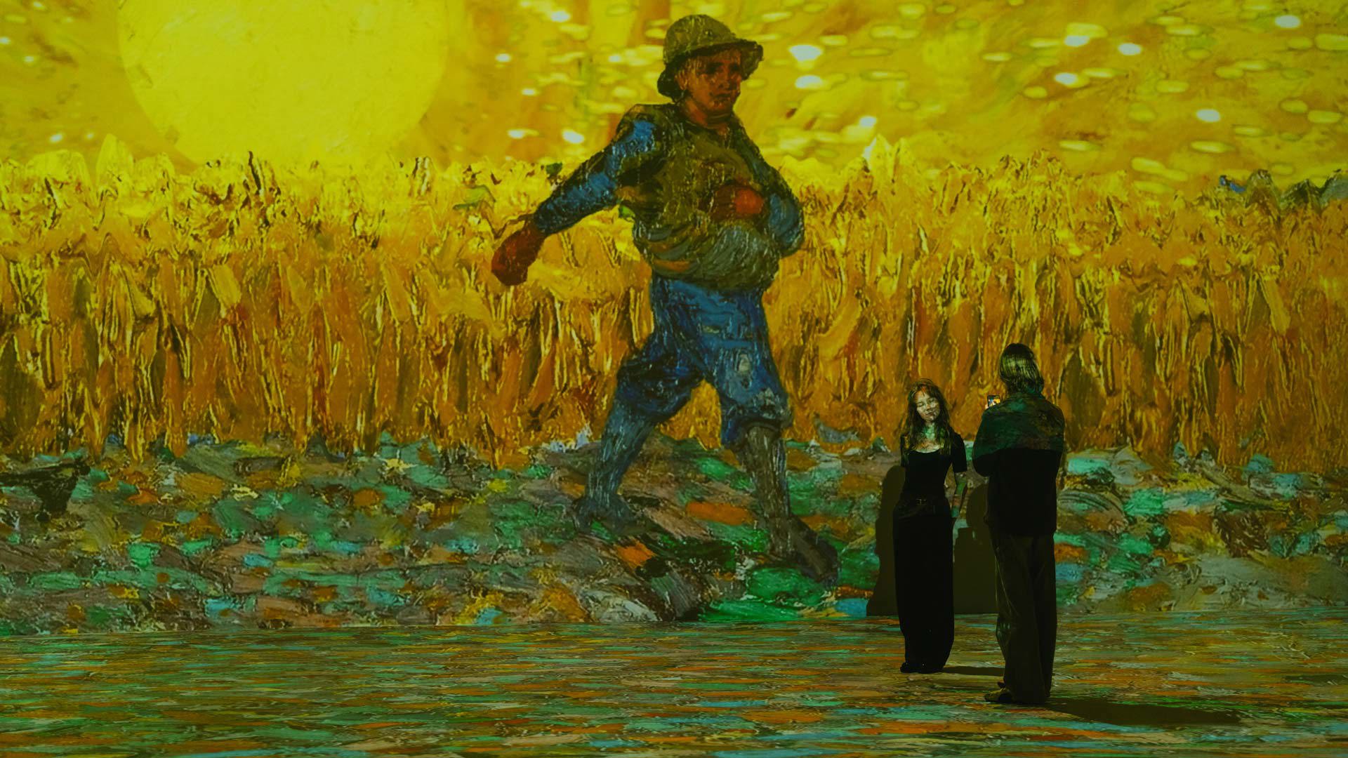 Dos adultos en una sala iluminada observando una proyección de un hombre al sol en el heno