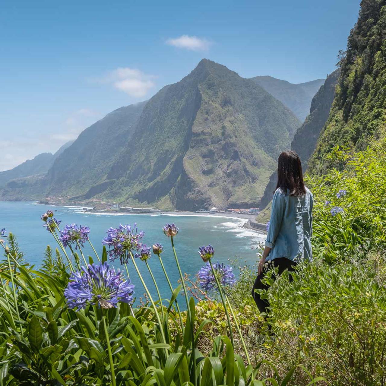 Mulher de costas contempla paisagem de natureza, mar e montanha.