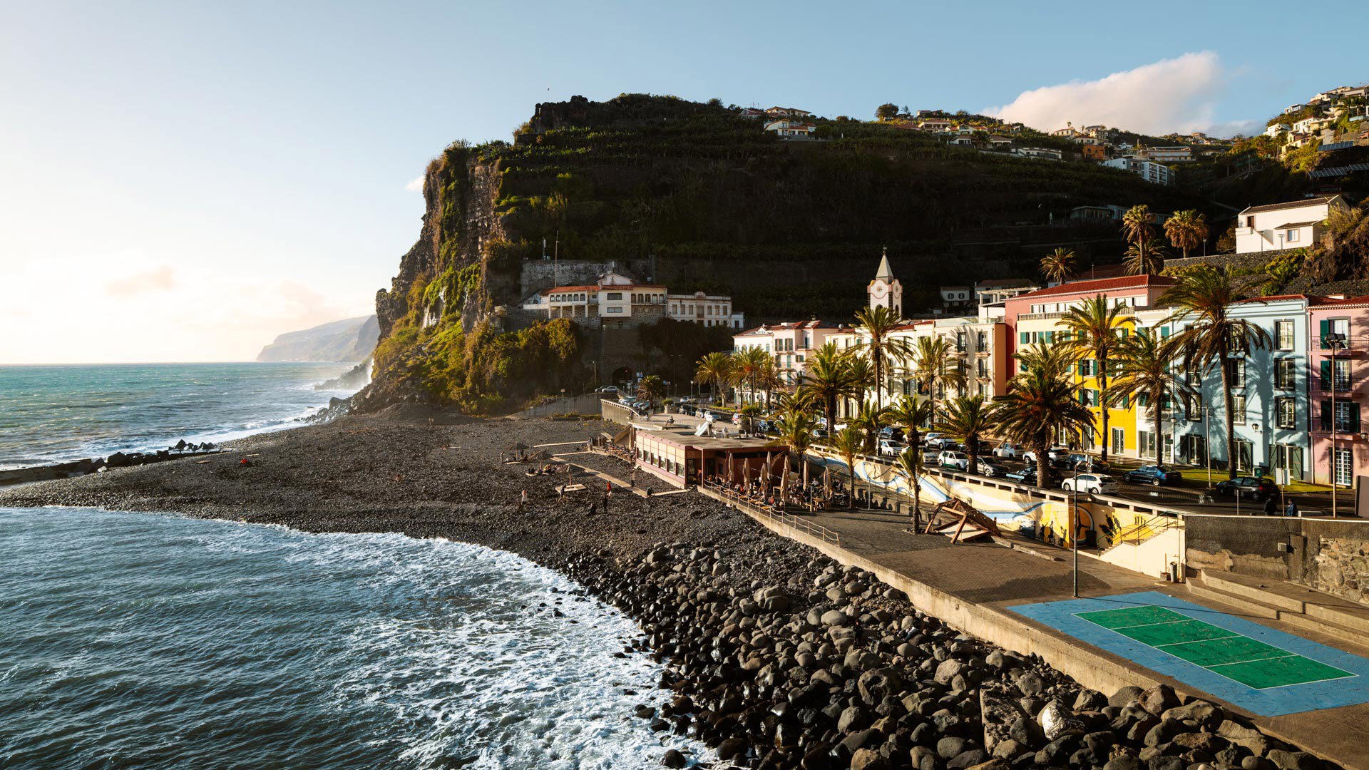 Plage de galets à Ponta do Sol, avec mer, bâtiments colorés et pente de Madère.
