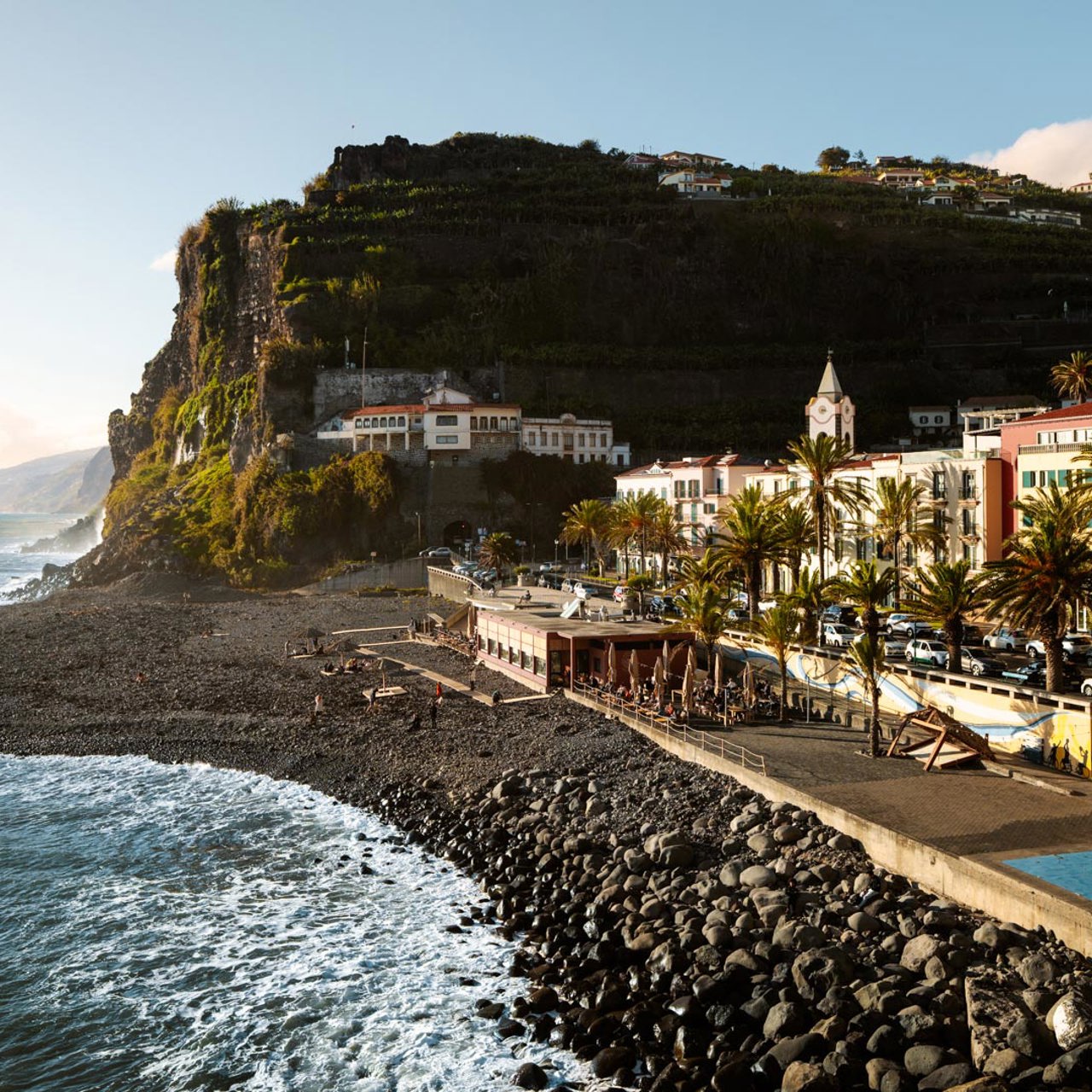 Plage de galets à Ponta do Sol, avec mer, bâtiments colorés et pente de Madère.