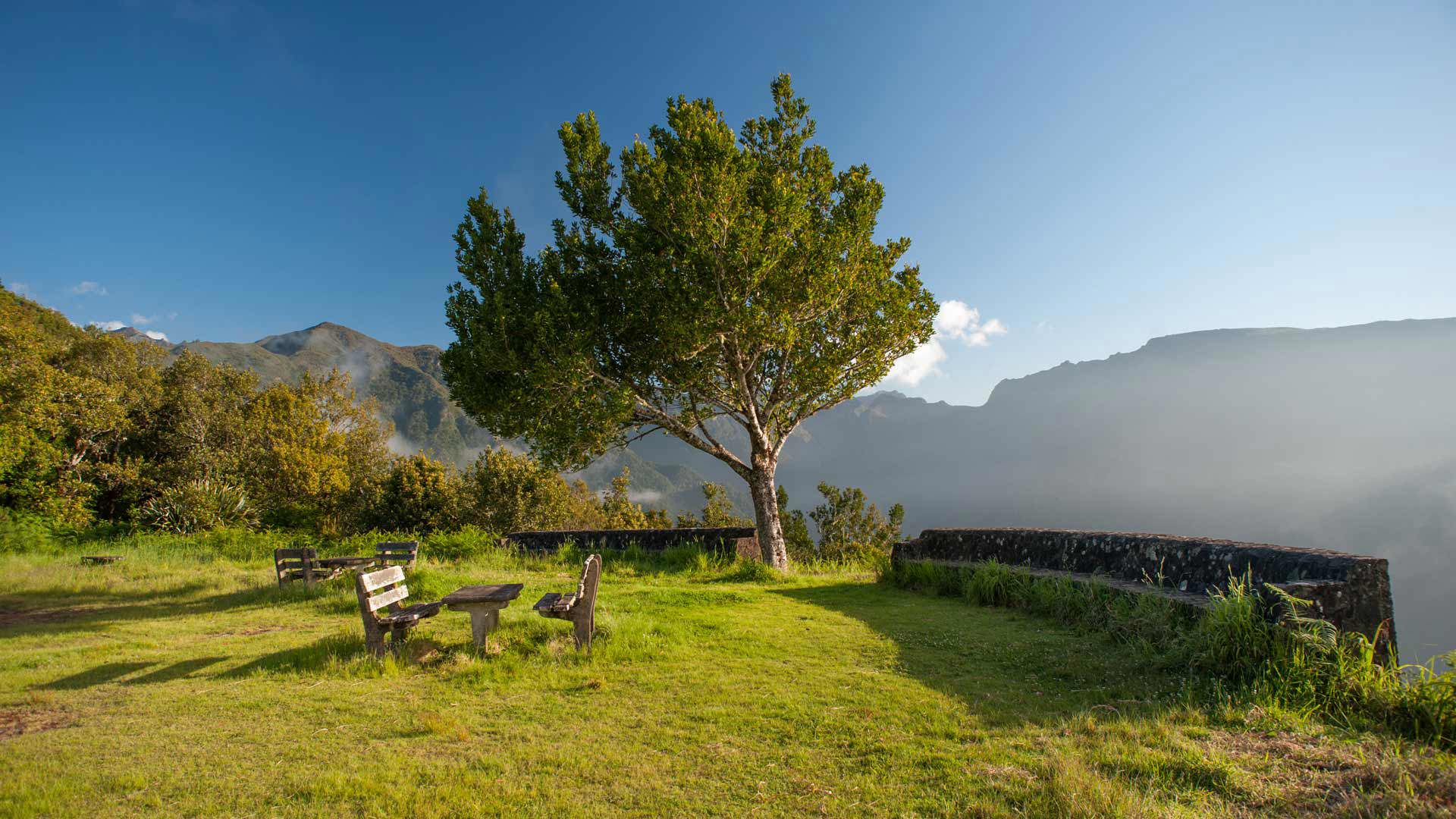 Miradouro com jardim, bancos de madeira e montanhas na Madeira.
