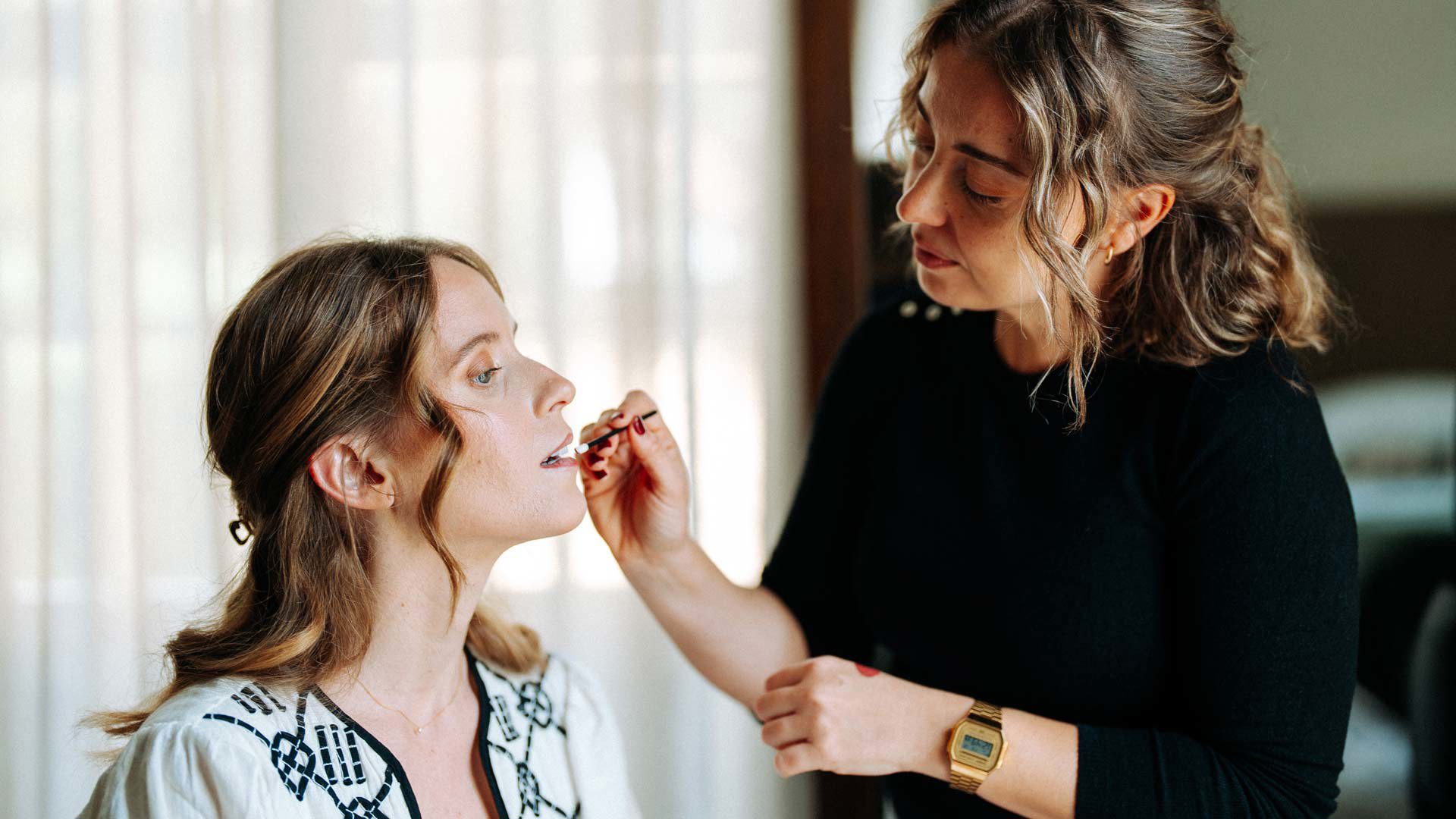 Makeup artist applying lipstick on the bride.