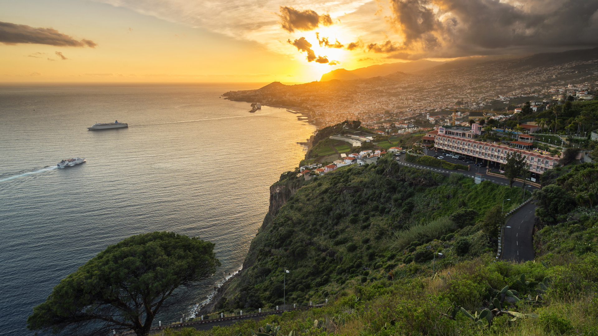 Sonnenuntergang über grüne Vegetation und Meer mit Booten auf Madeira.