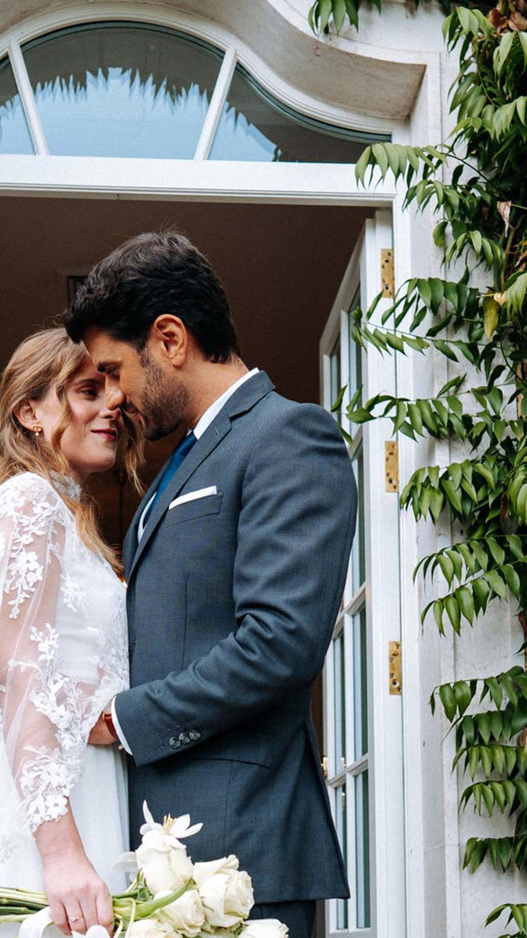 Bride and groom by a door, with shrubs in the background.