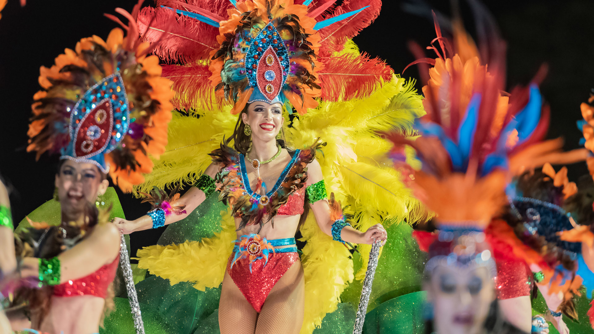 Personnes dansant lors du cortège de Carnaval avec des costumes colorés à plumes.