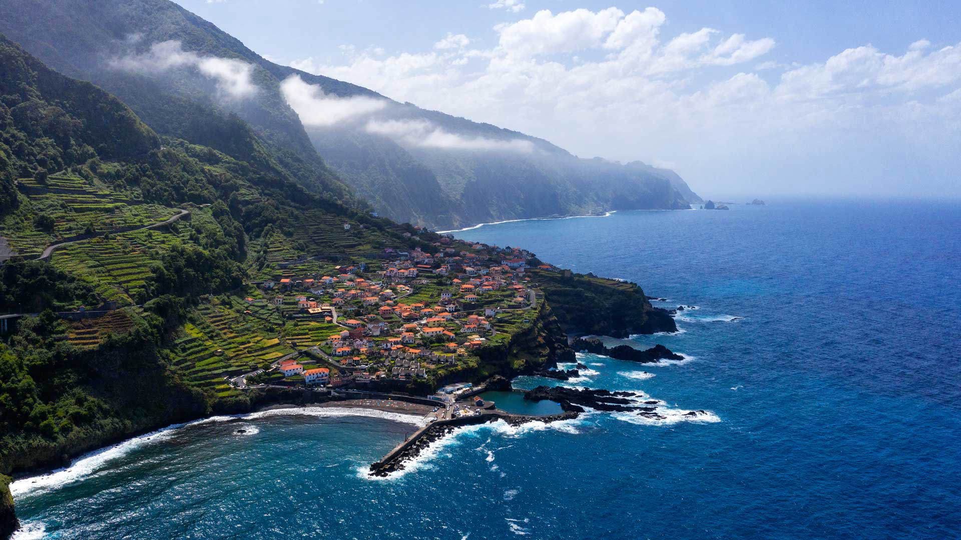 Mountain with slope, houses and pier by the sea in Madeira.
