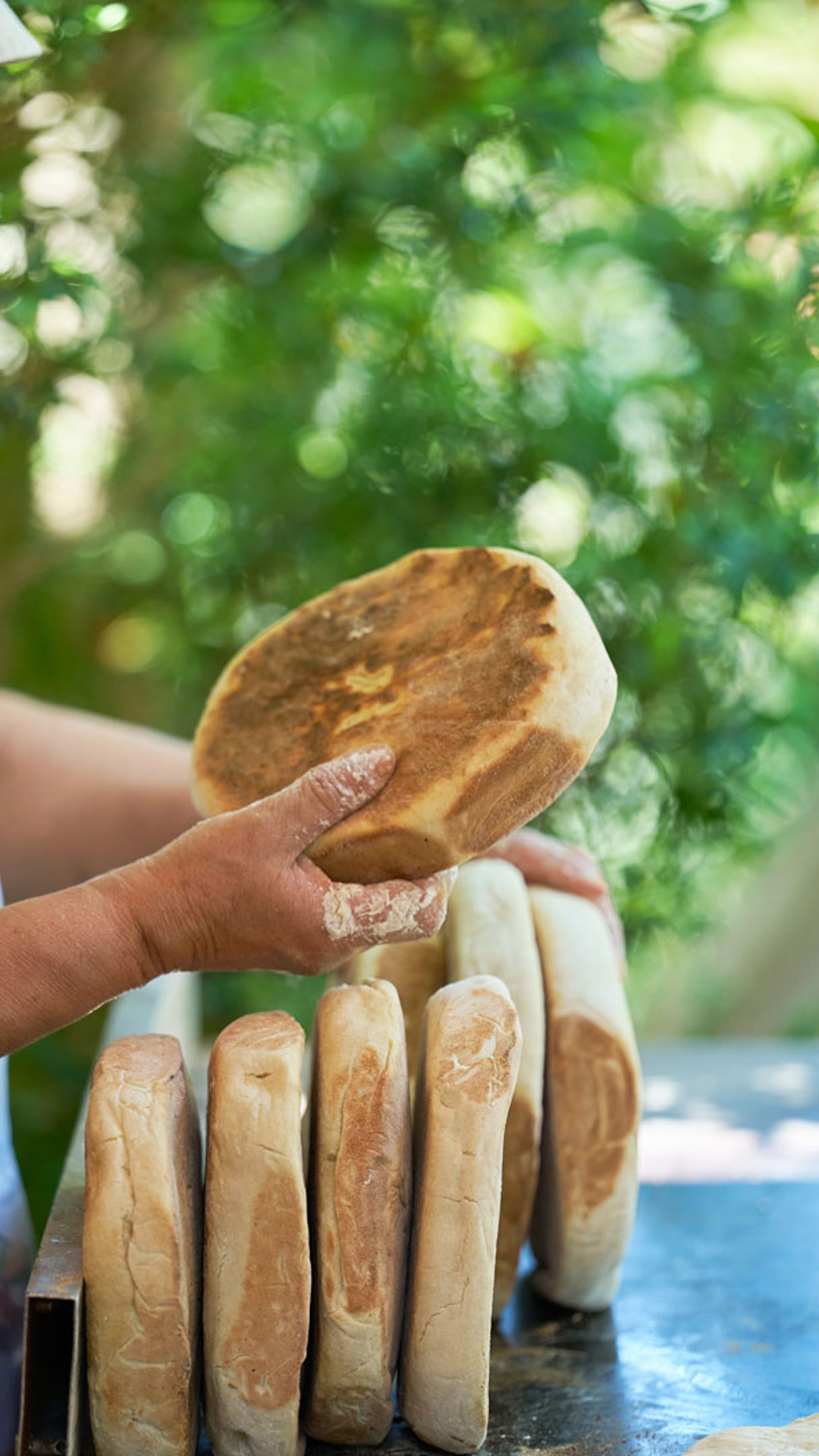 Mujer preparando bolos do caco en una plancha tradicional.